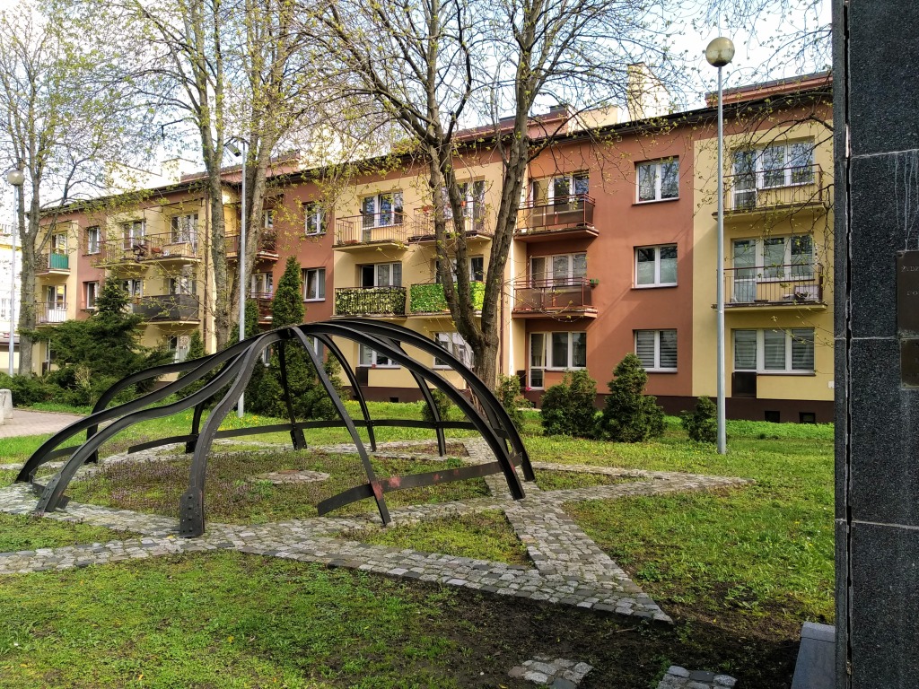 A warped metal frame of a dome sits atop a paved Star of David in a small garden.