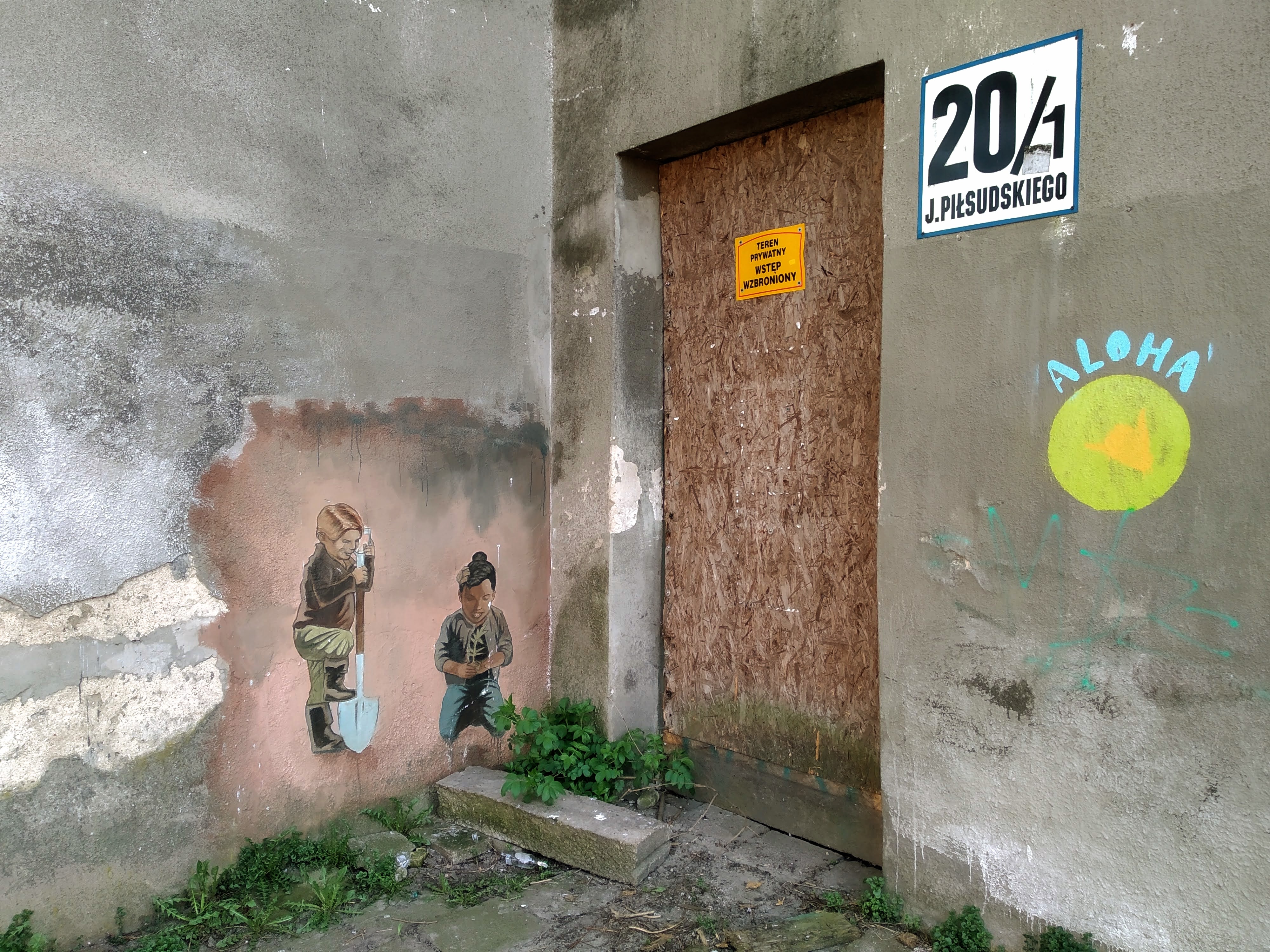 A boarded doorway at right-angles to a mural of one boy kneeling and another digging. 