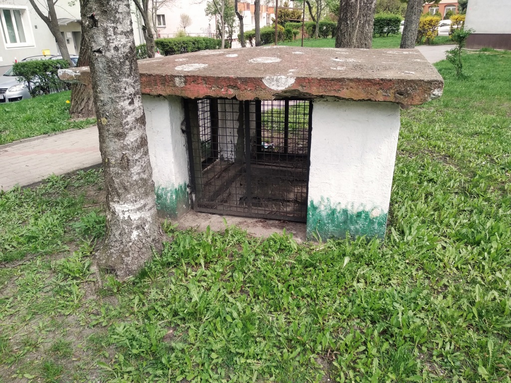 In a residential area, a small concrete access point to a bunker is in the grass.