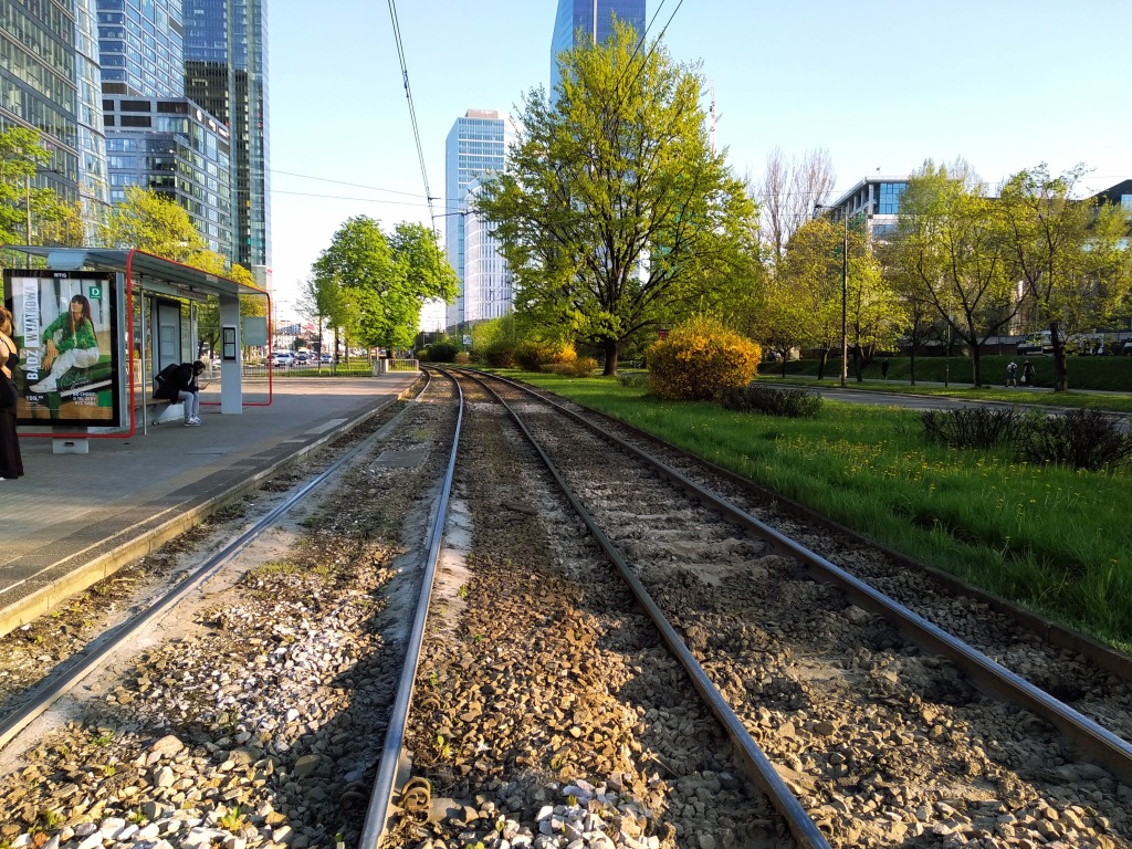 Looking down the rails through trees at skyscrapers from Warsaw's Muzeum Powstania Warszawskiegot tram stop.