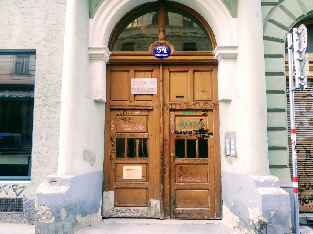 A big wooden door with graffiti under the number 54 on a blue enamel plaque.