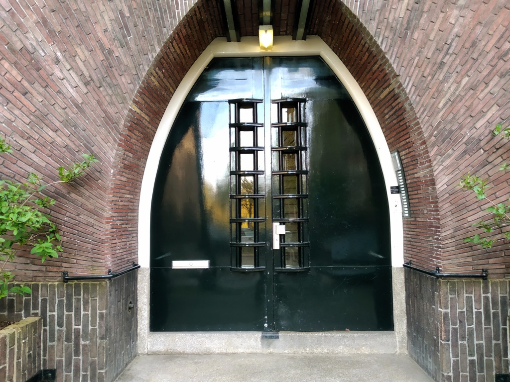 An arched black metal door surrounded by arched red brickwork that fans from it giving an illusion of movement.