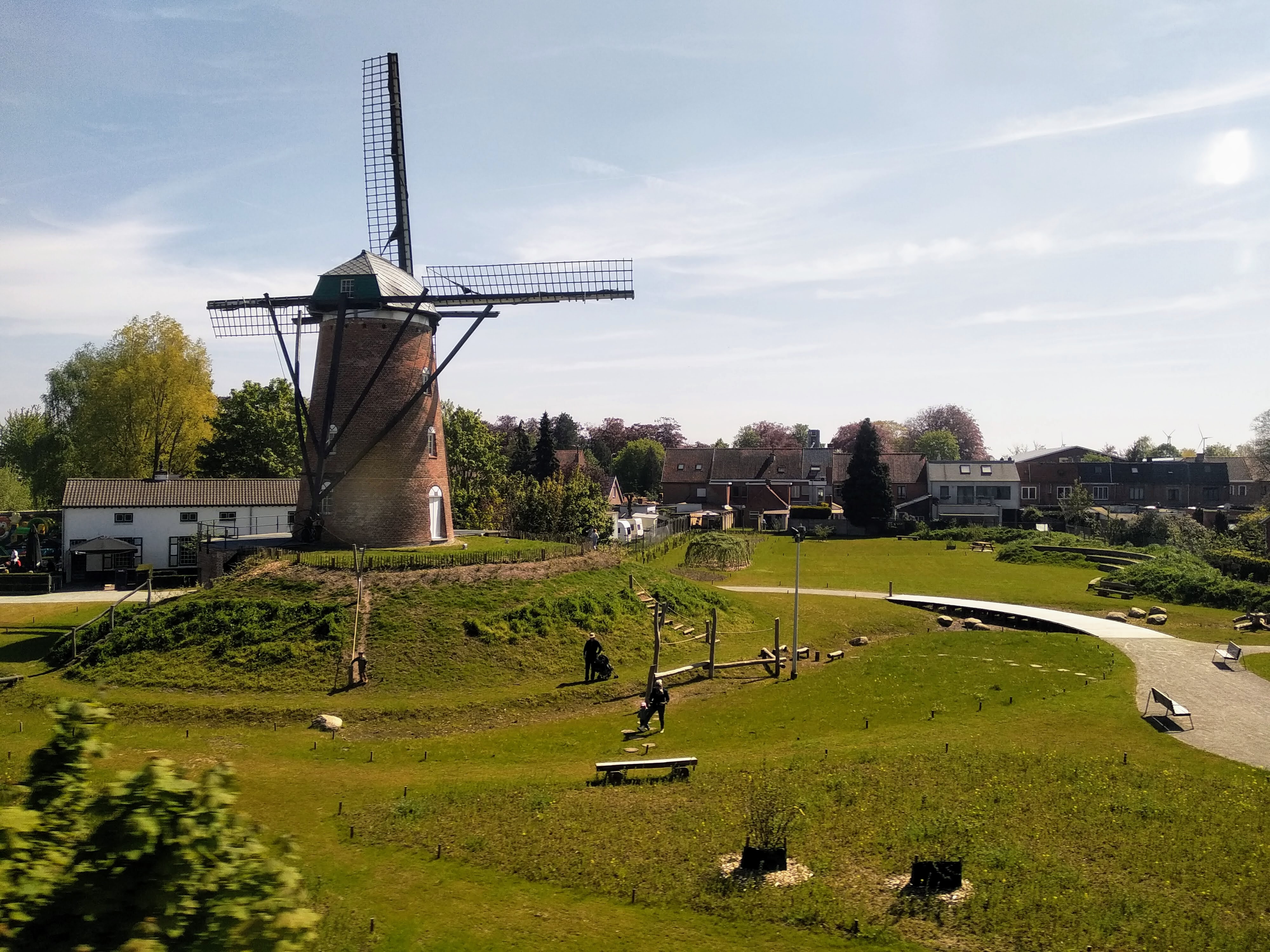 A stone windmill on a little grassy knoll in a park surrounded by residential Belgium.
