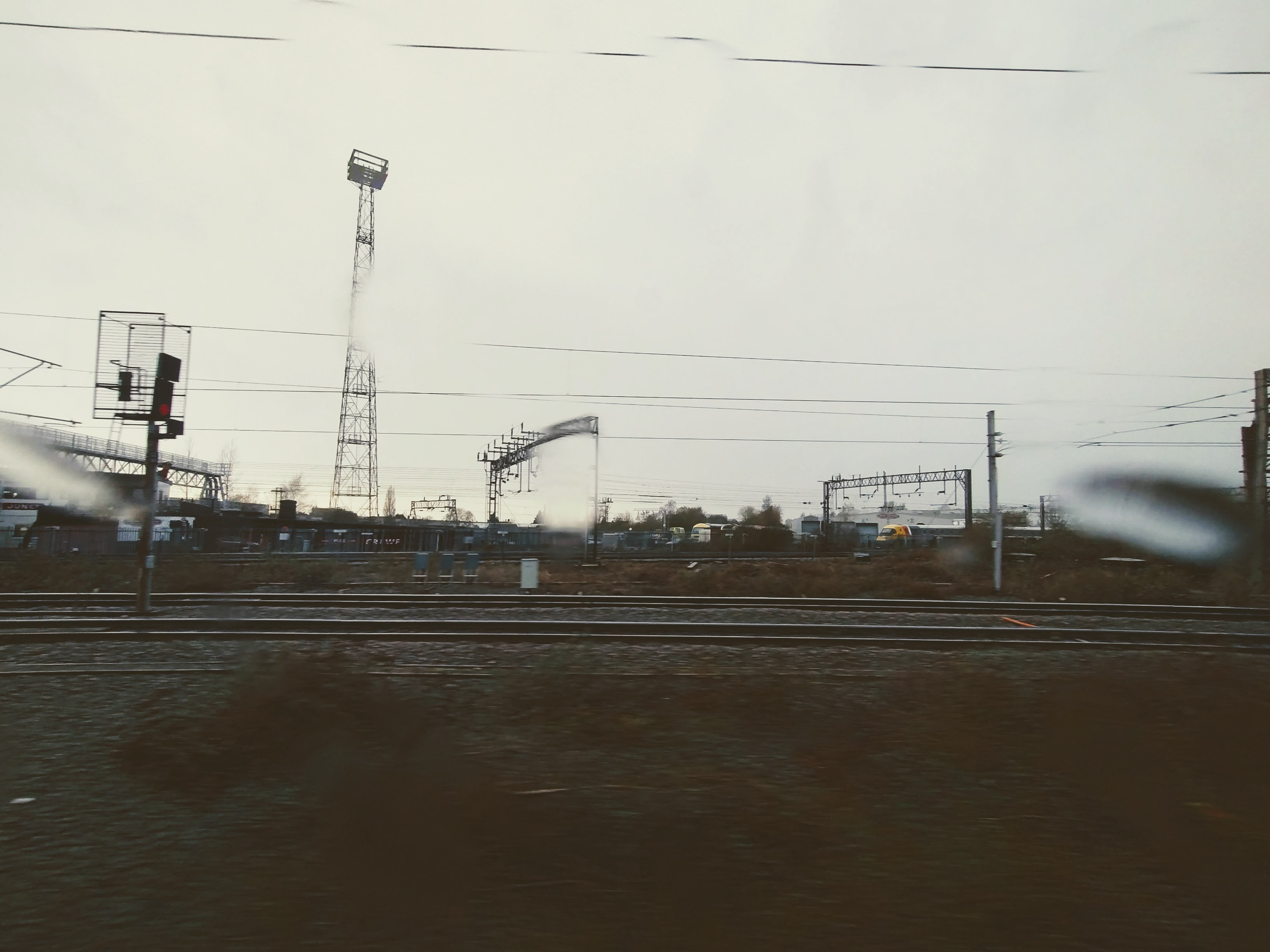 A photograph of a grey landscape taken through a wet window just outside Crewe. Two tracks run along the horizon. In the background can be seen the Advanced Passenger Train.