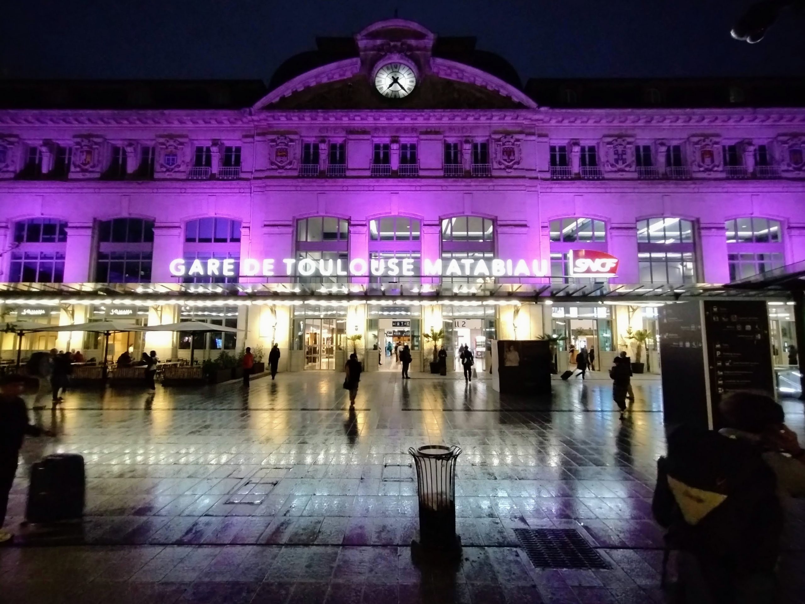The façade of Toulouse Matabiau railway station at night, bathed in purple light.