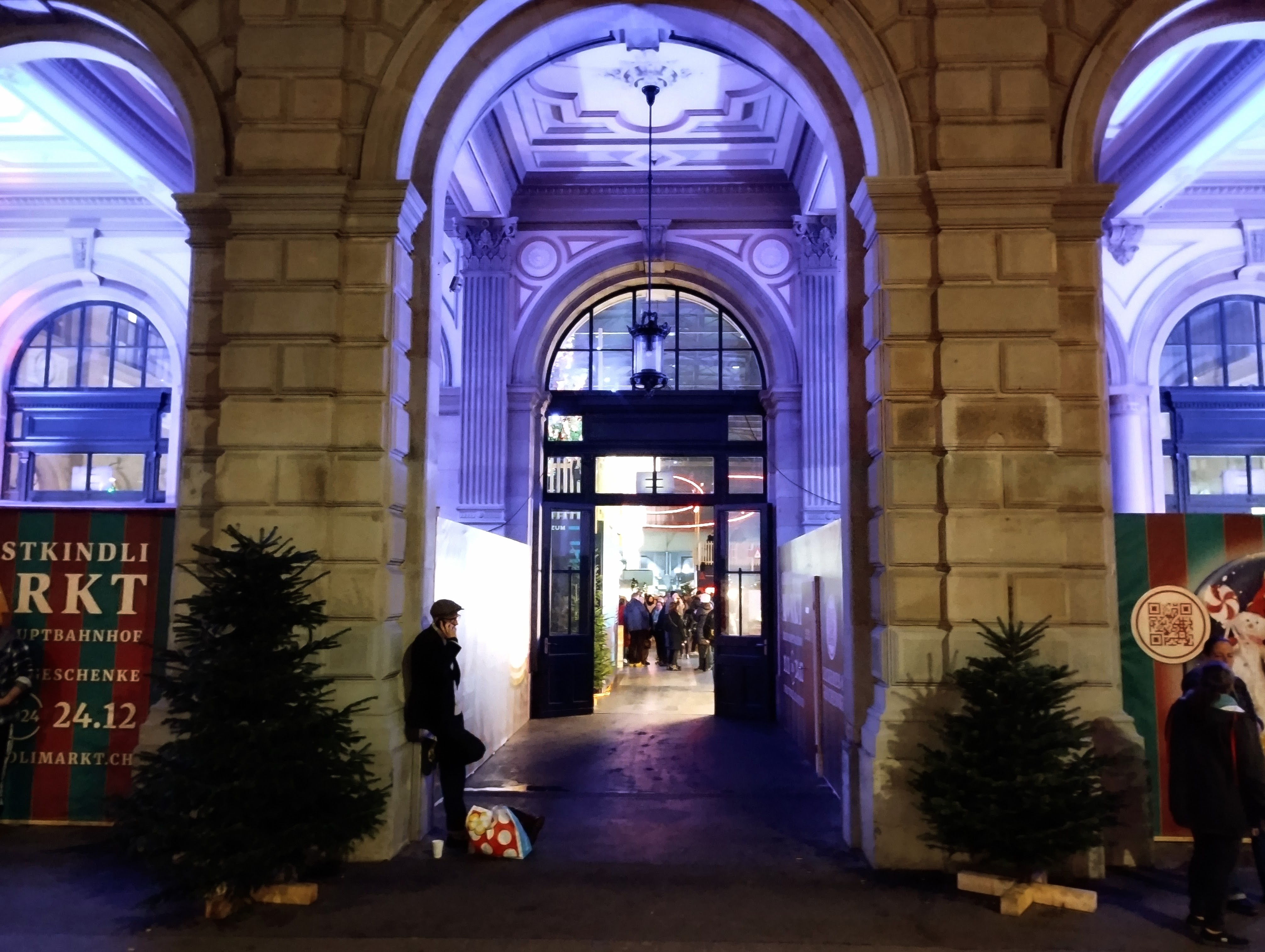 An open door to Zurich main station, behind a colonnade illuminated in lilac.