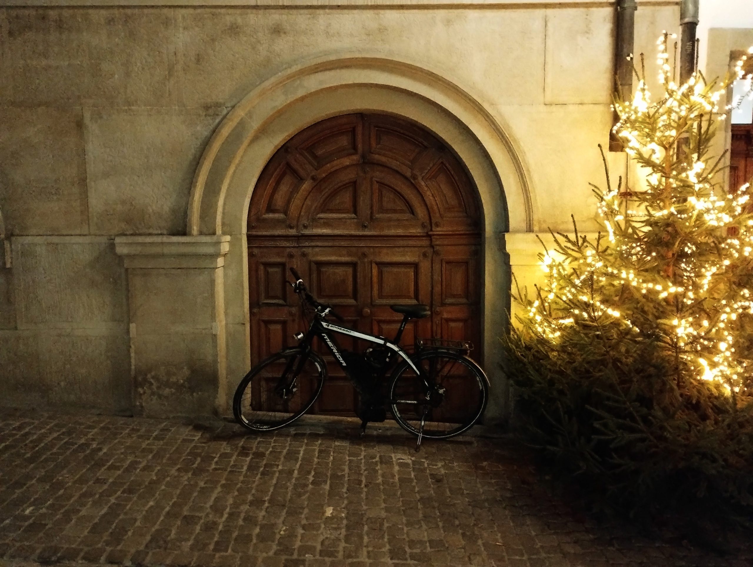A bicycled in front of small wooden door in an arch next to a Christmas tree.