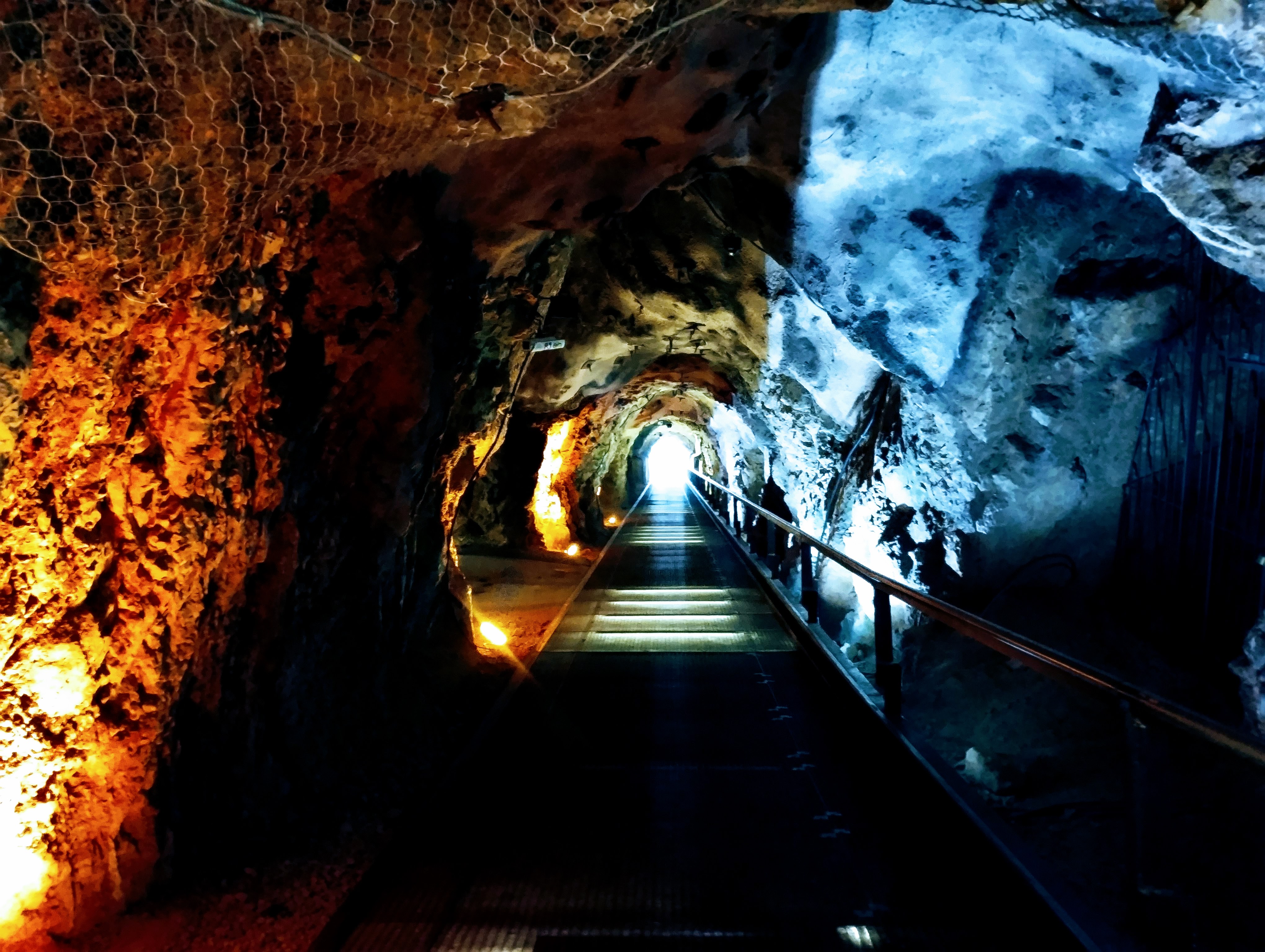 A tunnel through rock is made striking by the red and blue illuminations either side of the metal walkway.