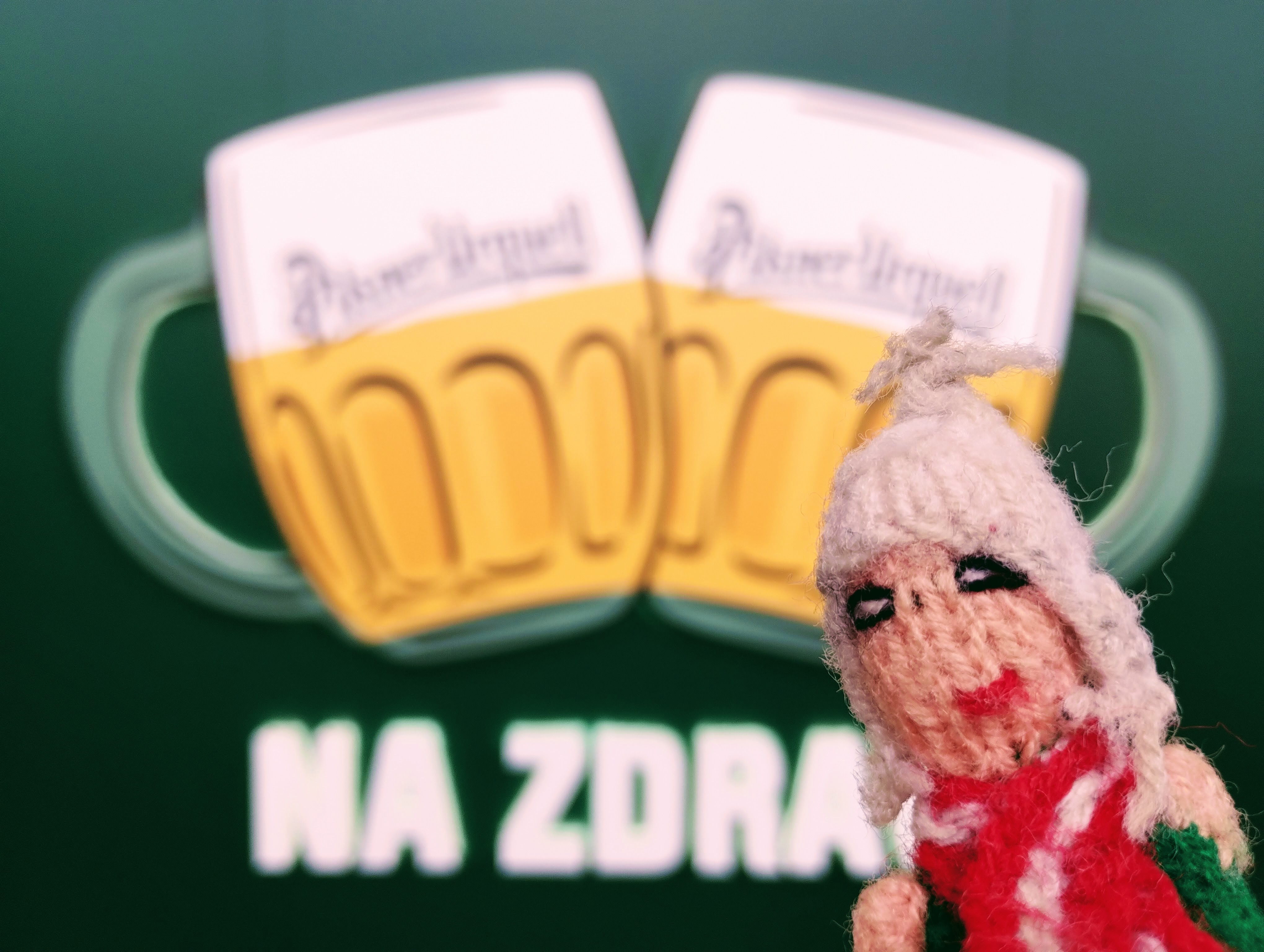 Puppet stands in front of a stylised image of two toasting glasses of Pilsner Urquell.