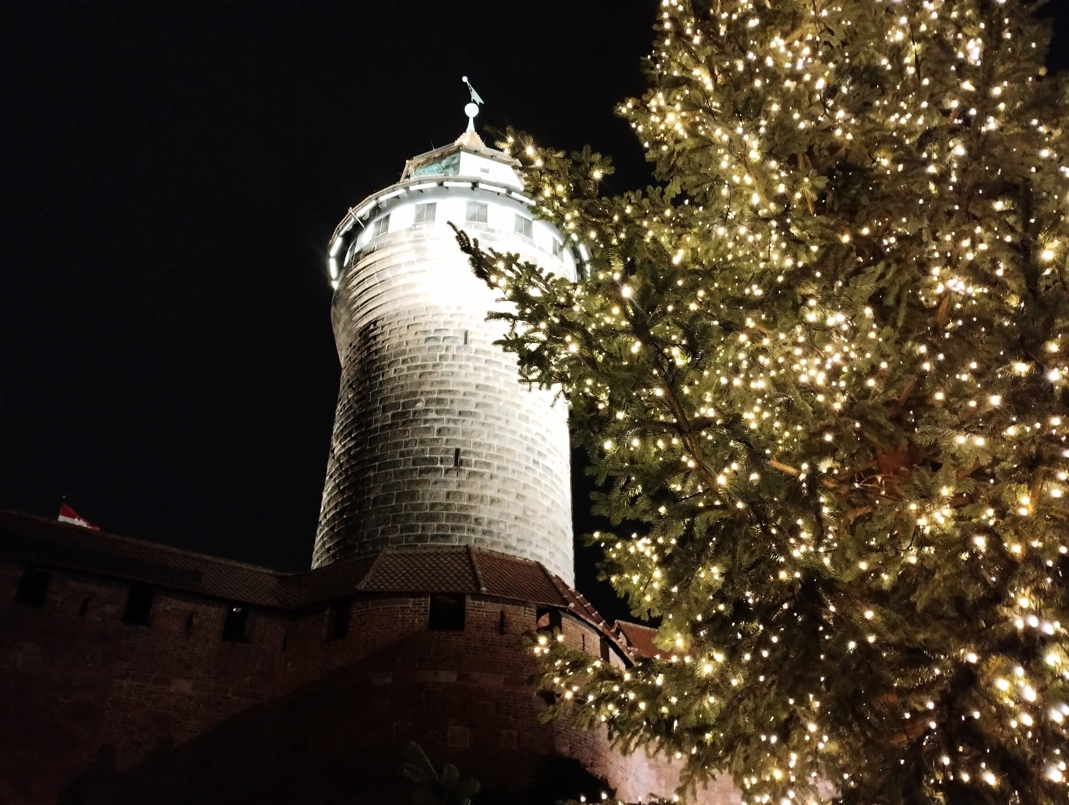 A grey stone tower behind an illuminated Christmas tree.