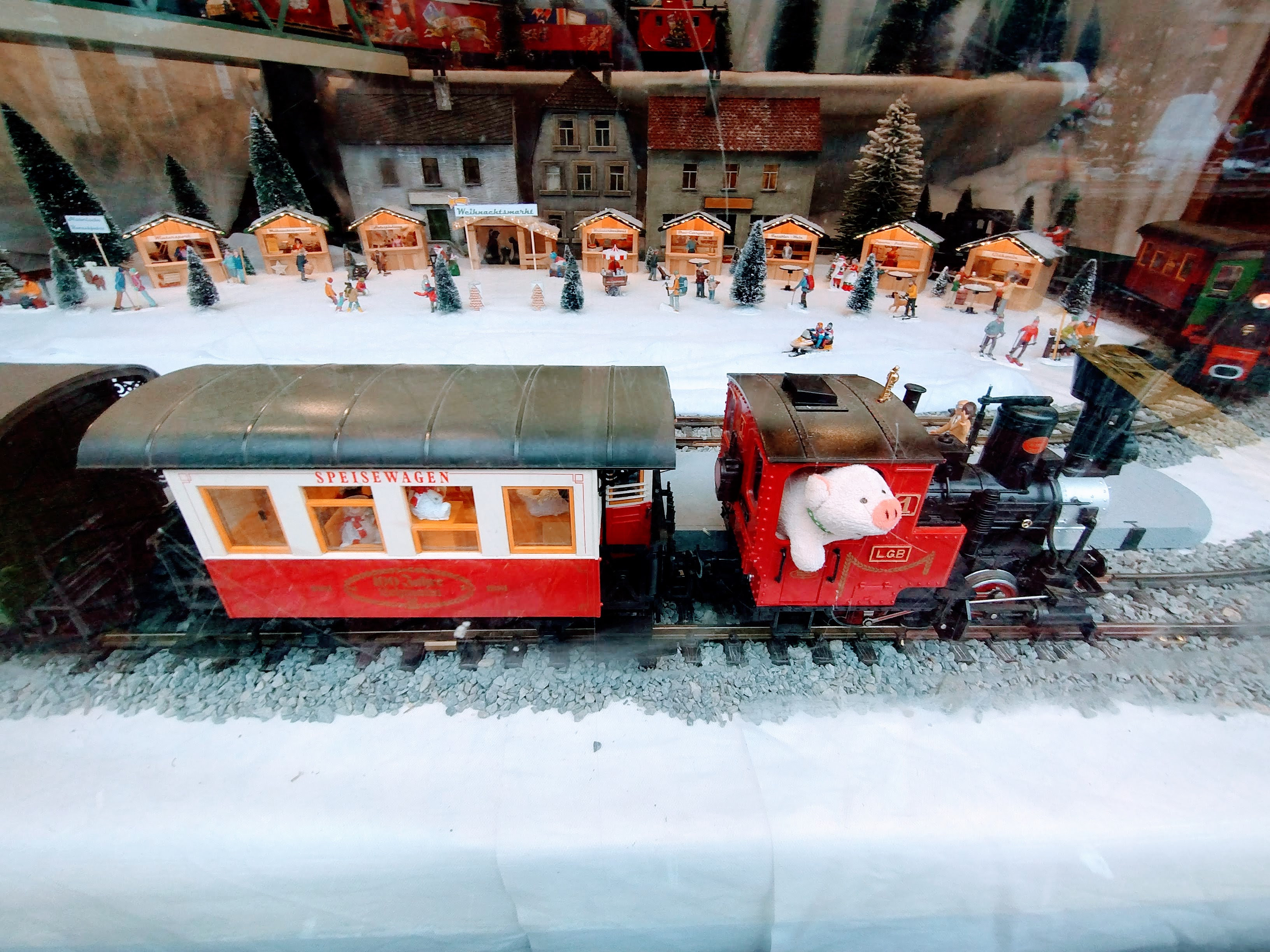 A fluffy pig drives a train pulling a dining car in a festive model railway display.