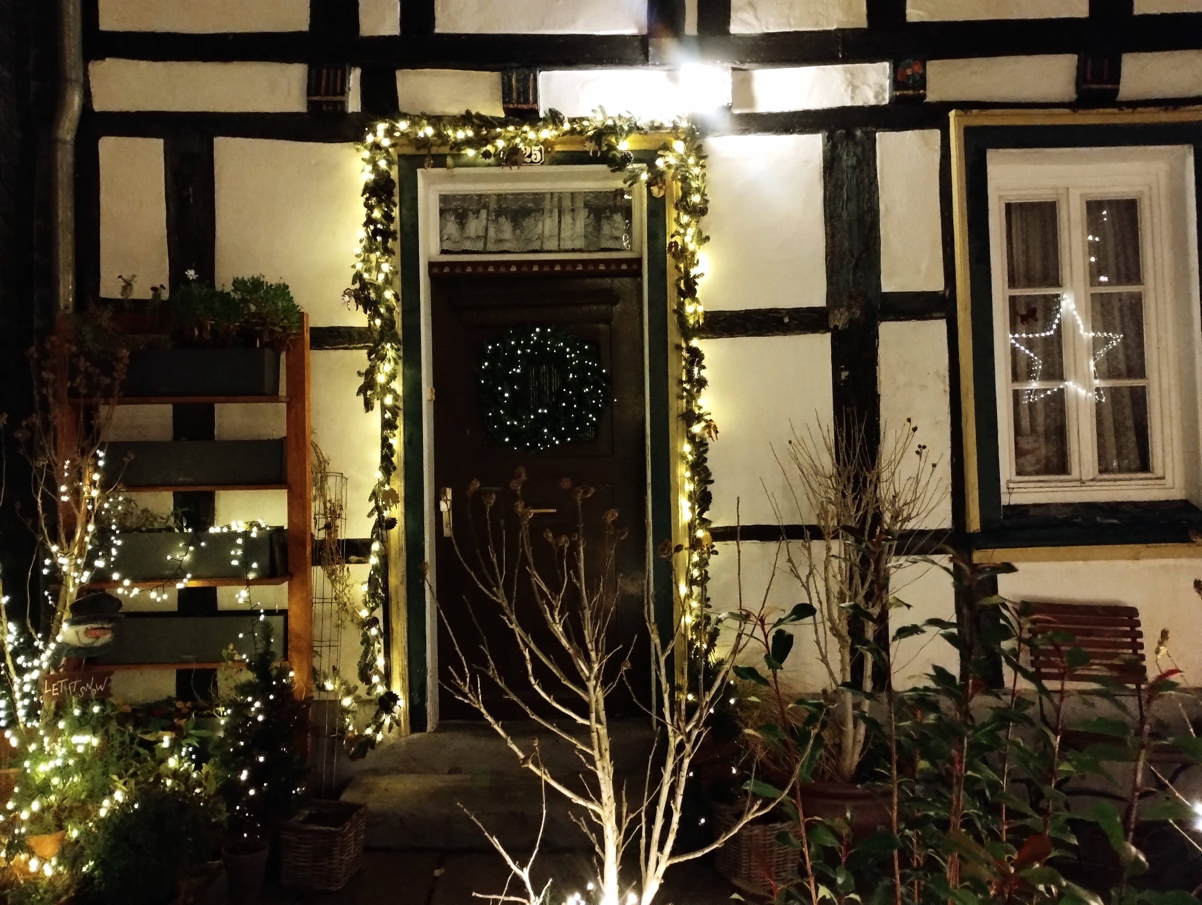 The wooden front door of a black and white house, decorated for Christmas with lights and a wreath.