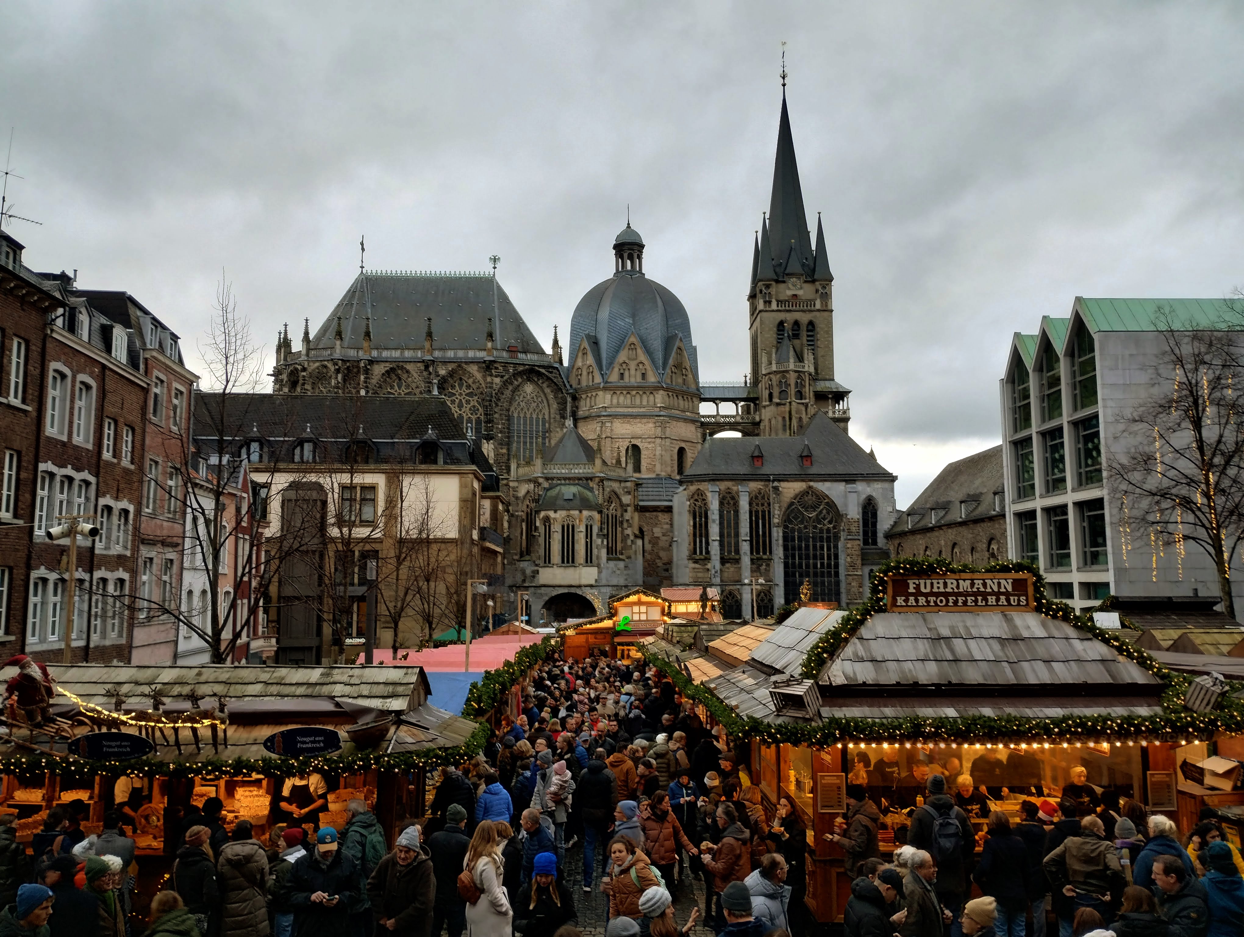 The cathedral in Aachen behind a busy Christmas market in a square.