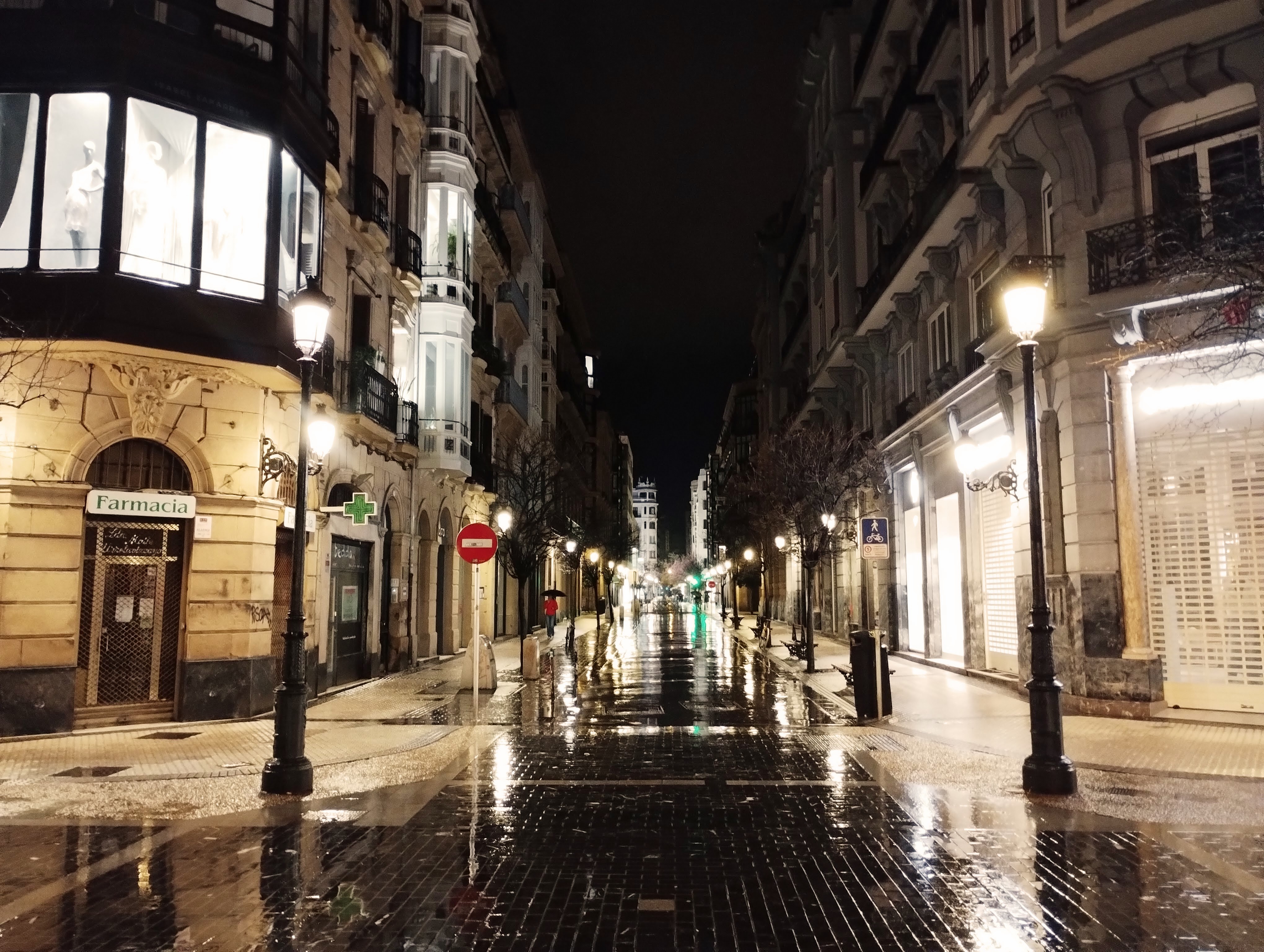 A wet street reflects light from street lights flanking a pedestrian street in Saint Sebastián.