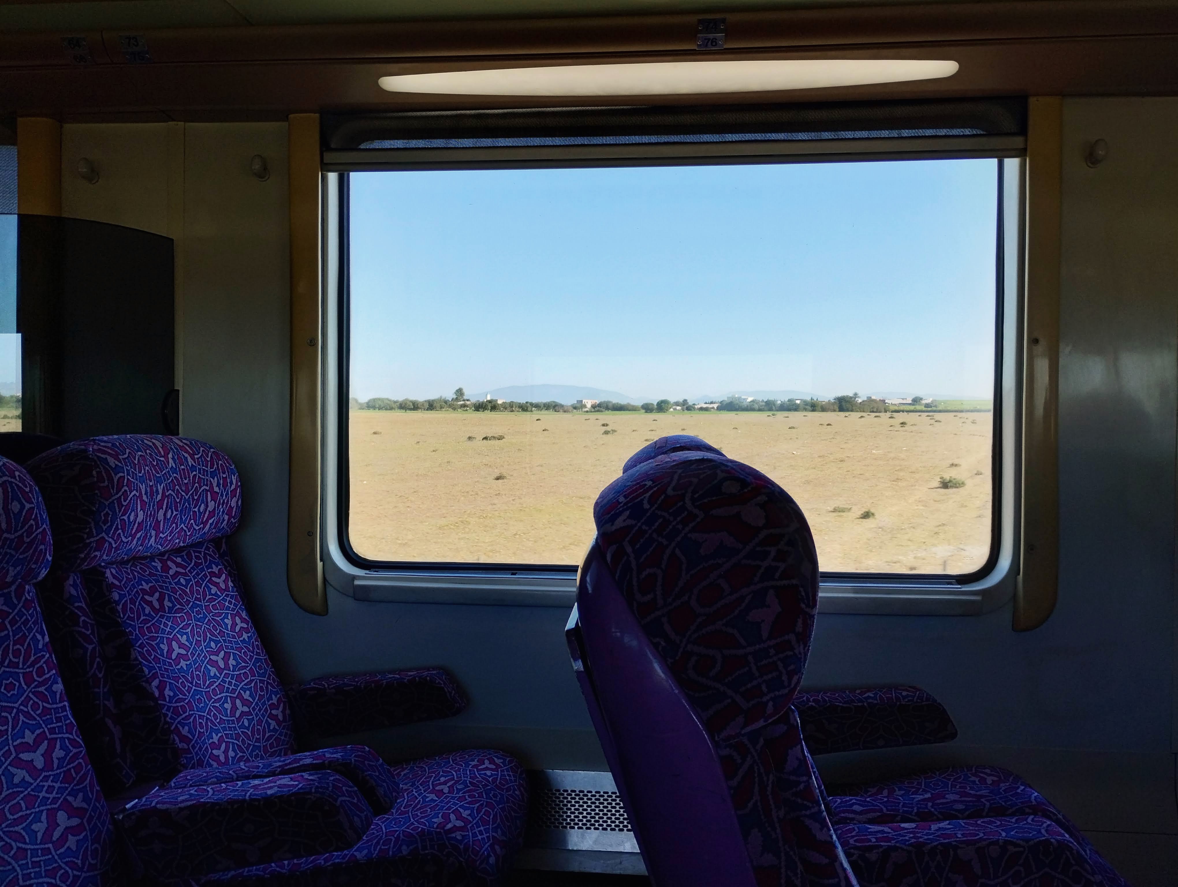 A dry Moroccan landscape passes a train window.