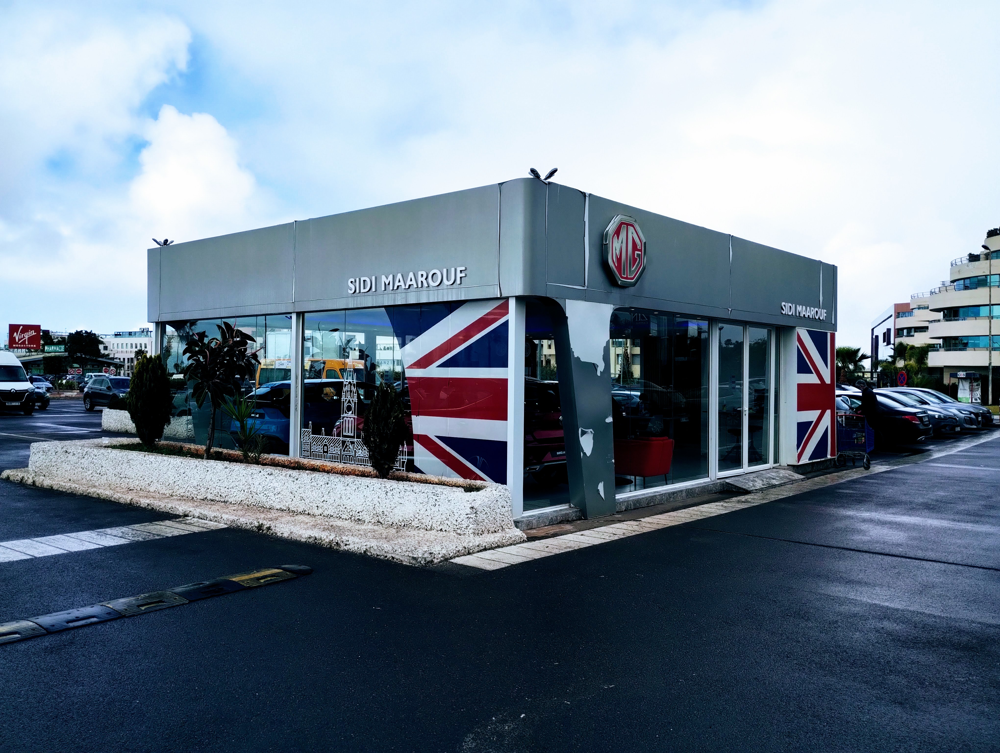 MG car dealership in a car park in Sidi Maarouf, with the Union flag design on the side, and the text "SIDI MAAROUF" on the facade above a pair of glass doors.
