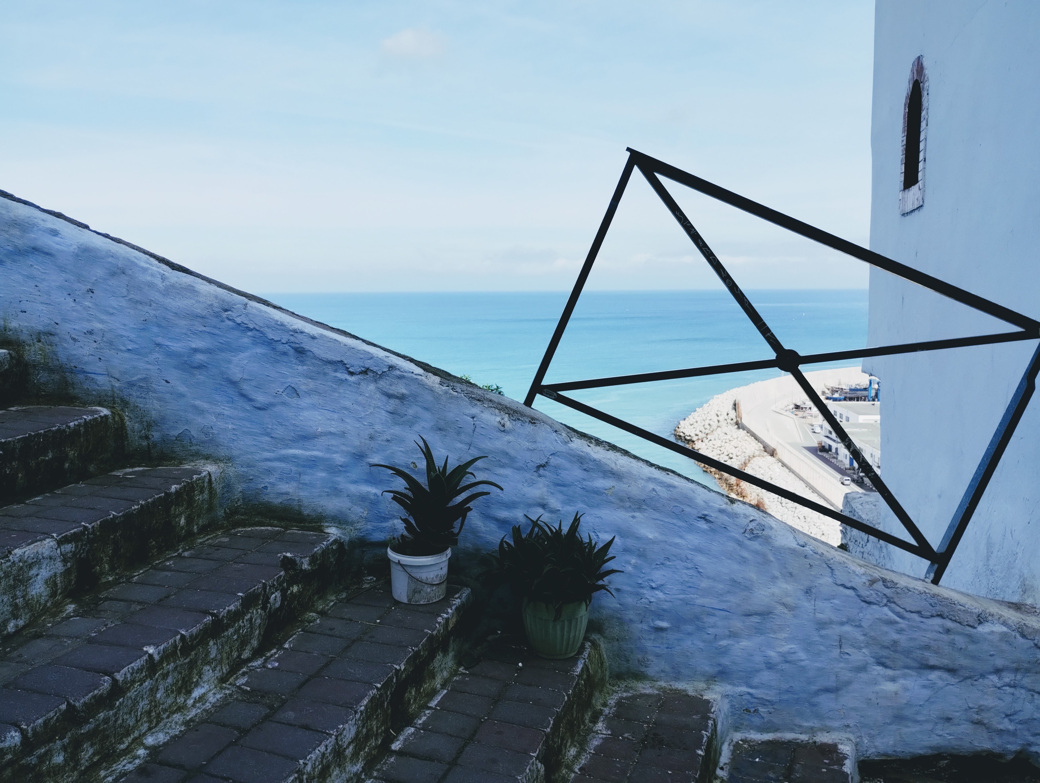 The Strait of Gibraltar seen through metal railings angled up a white-walled staircase.
