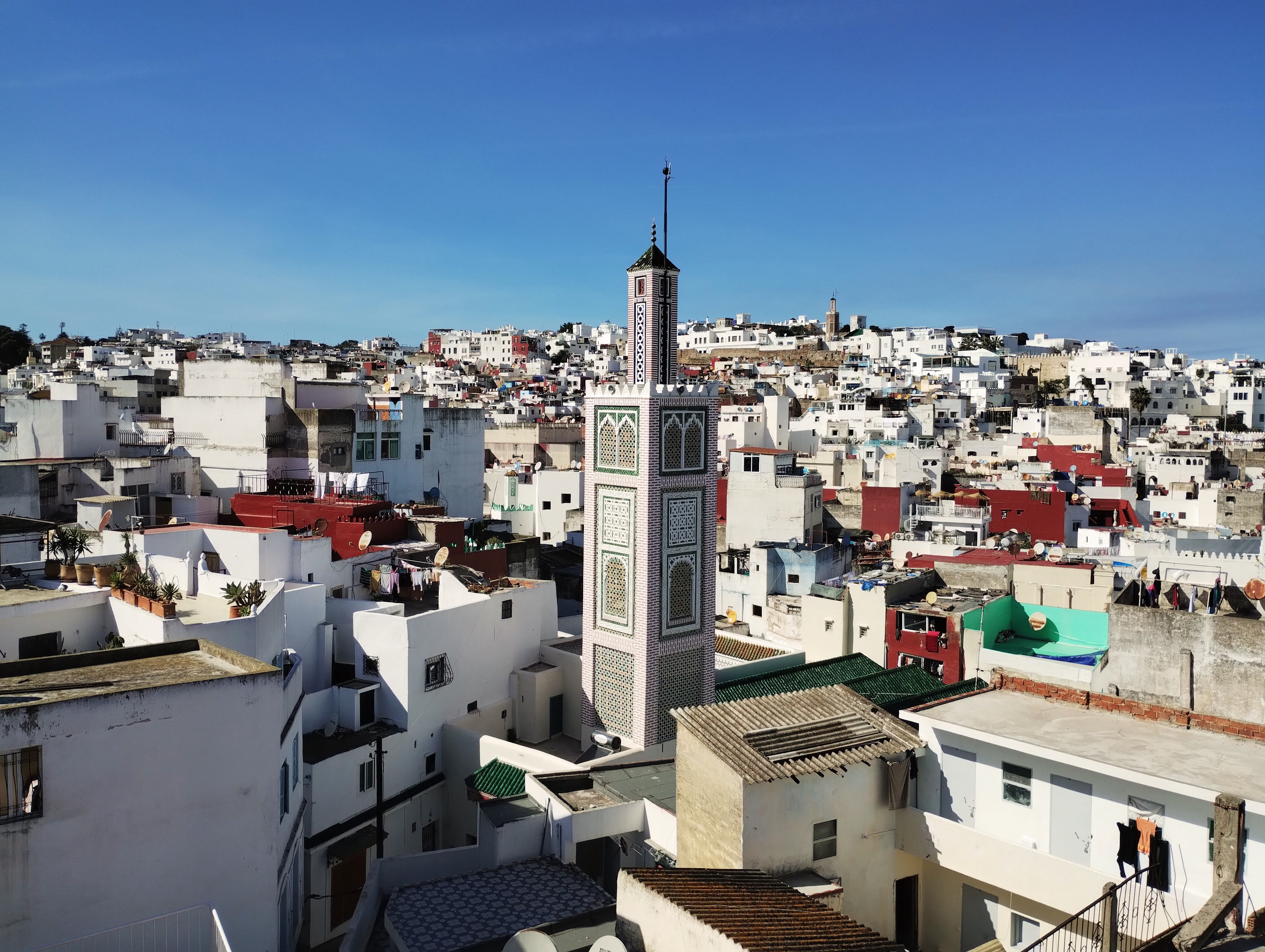The red, white, and green minaret of the Jedida Mosque above the white flat-roofed houses of Tangier.