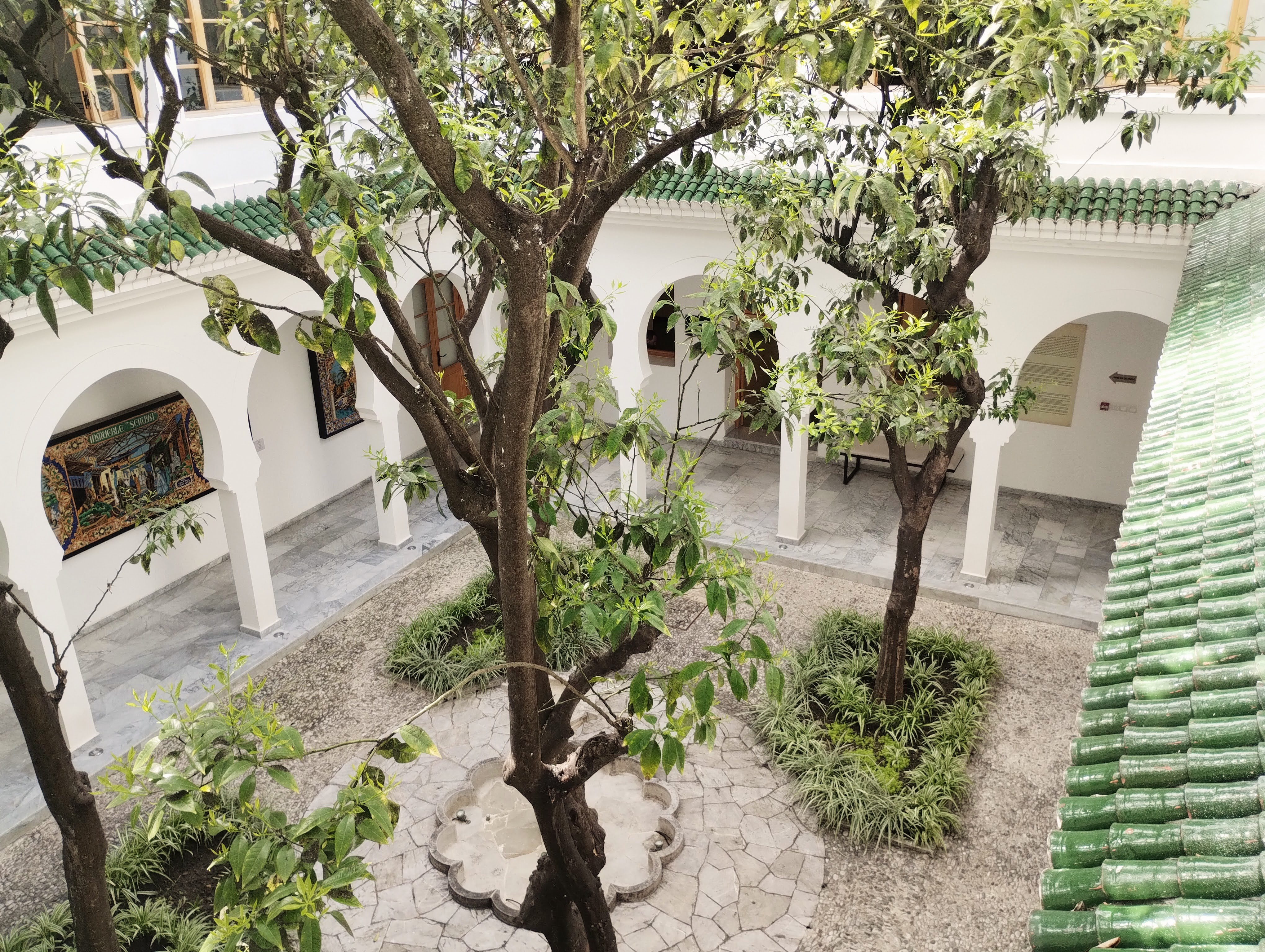 Trees in the internal courtyard of a white Moroccan building with green tiled roof.