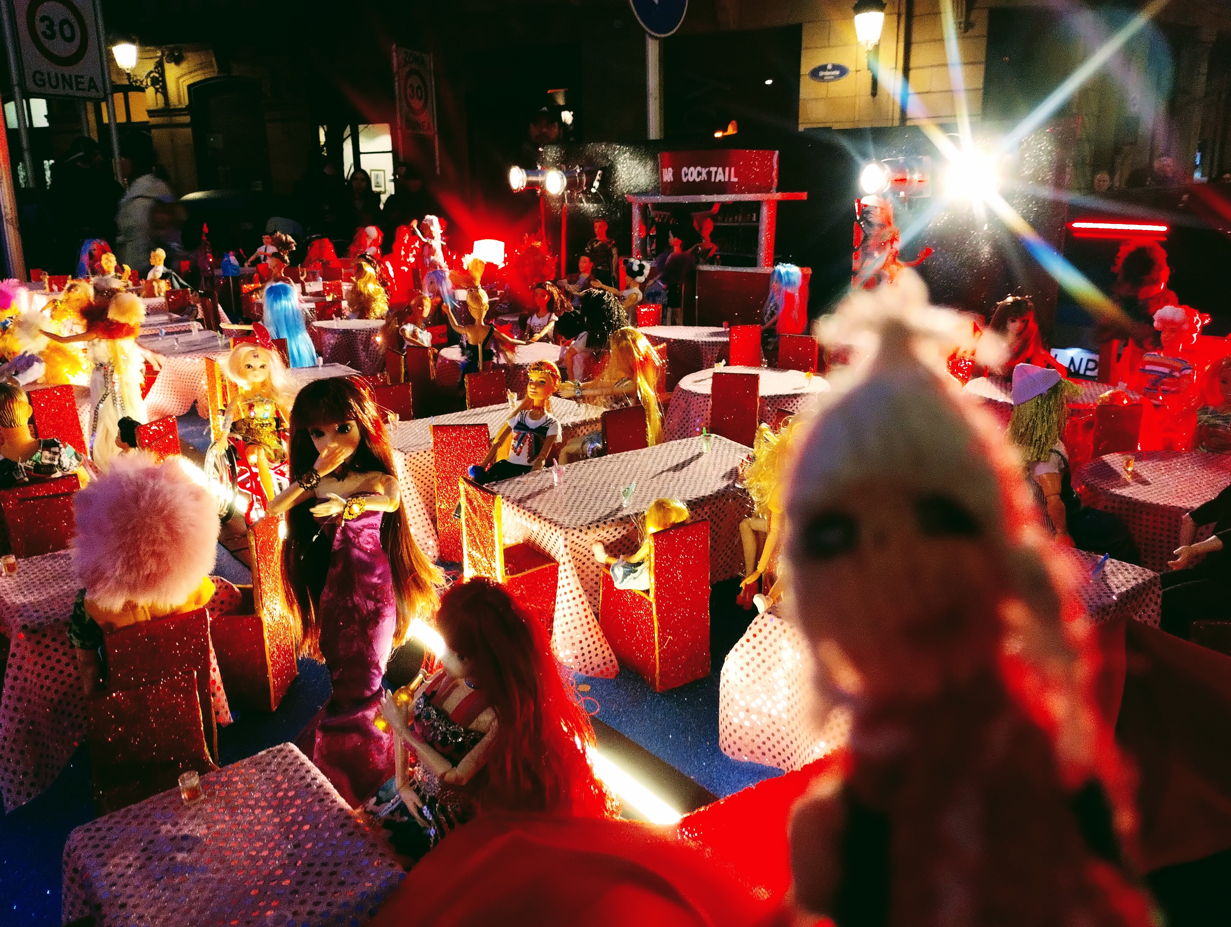 An exuberant finger puppet mingles with partying Barbie dolls on a carnival float.