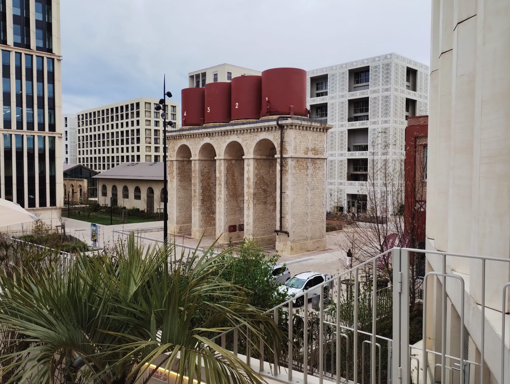 Four stone arches under numbered red cisterns among modern residential buildings.