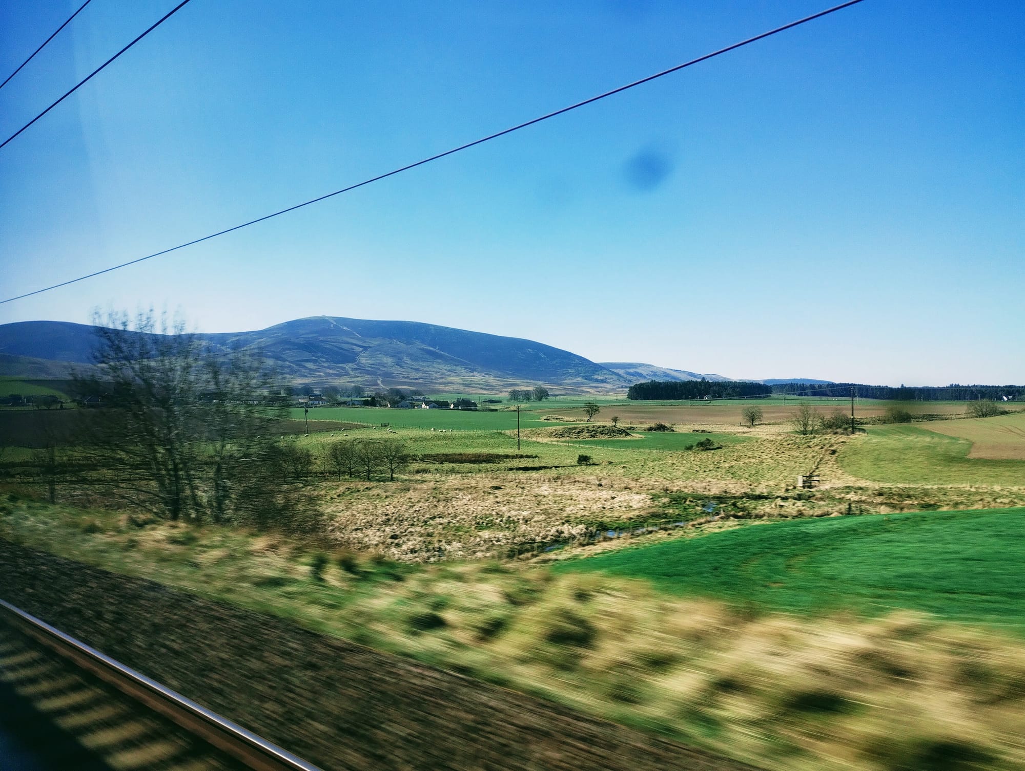 Green fields and mountains passing a train window.