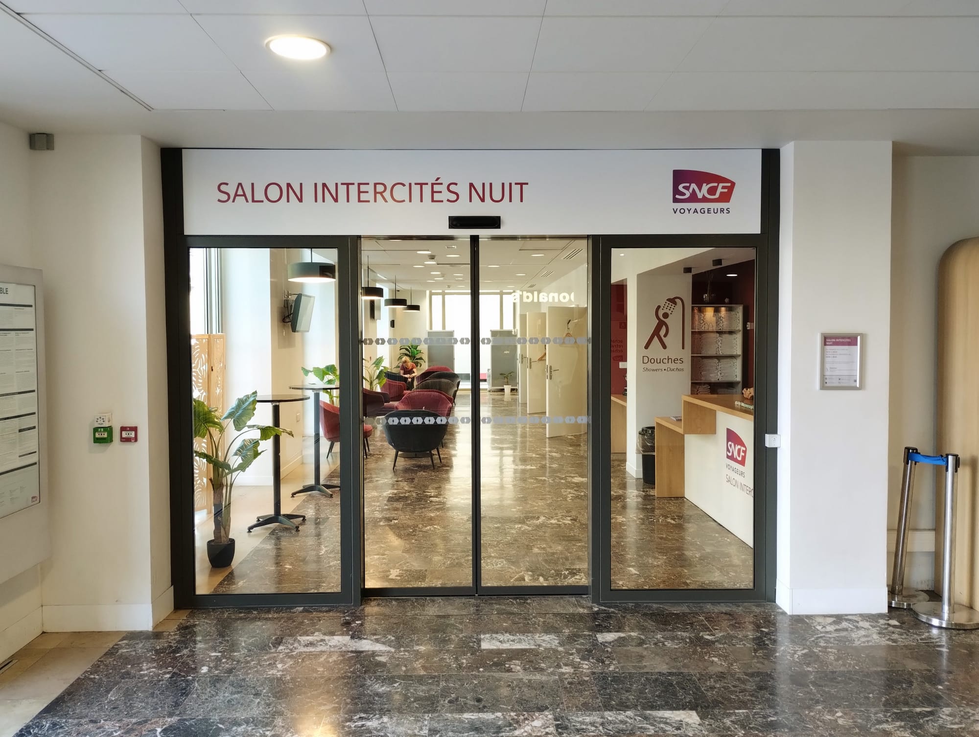 A photograph of the sliding glass doors into the 'salon intercitiés nuit' in Toulouse-Matabiau. We can see chairs and tables through the glass.