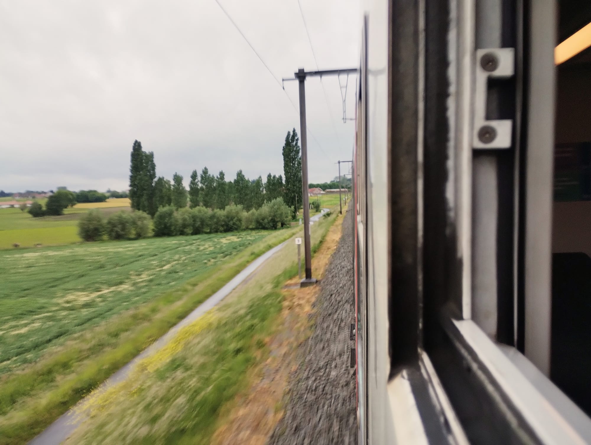 Looking towards the front of a train from the window of a trailing carriage, a view of track and passing farmland.