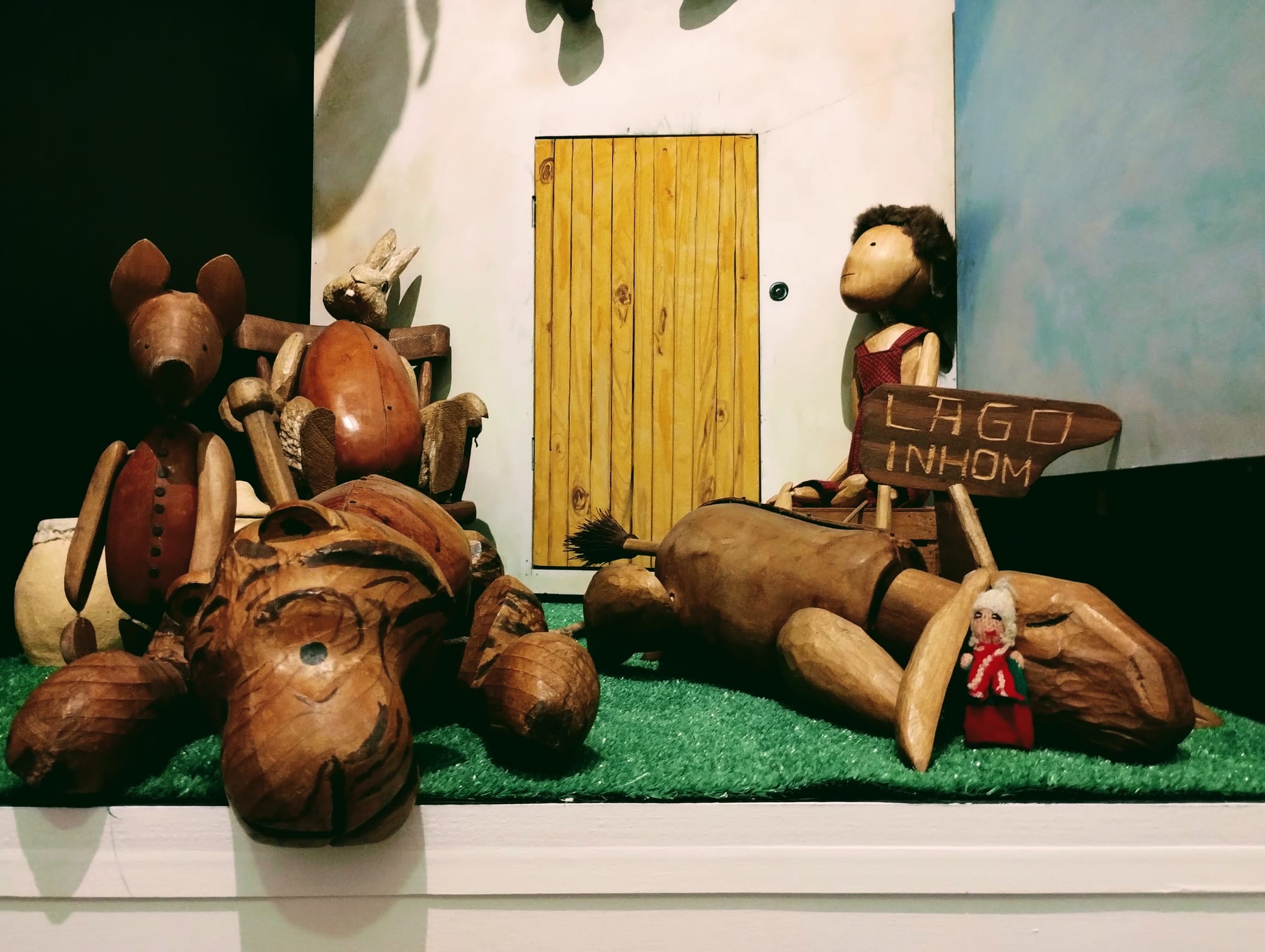 A scene featuring carved wooden representations of Piglet, Eeyore, Rabbit, and Winnie the Pooh, and a Peruvian finger puppet.