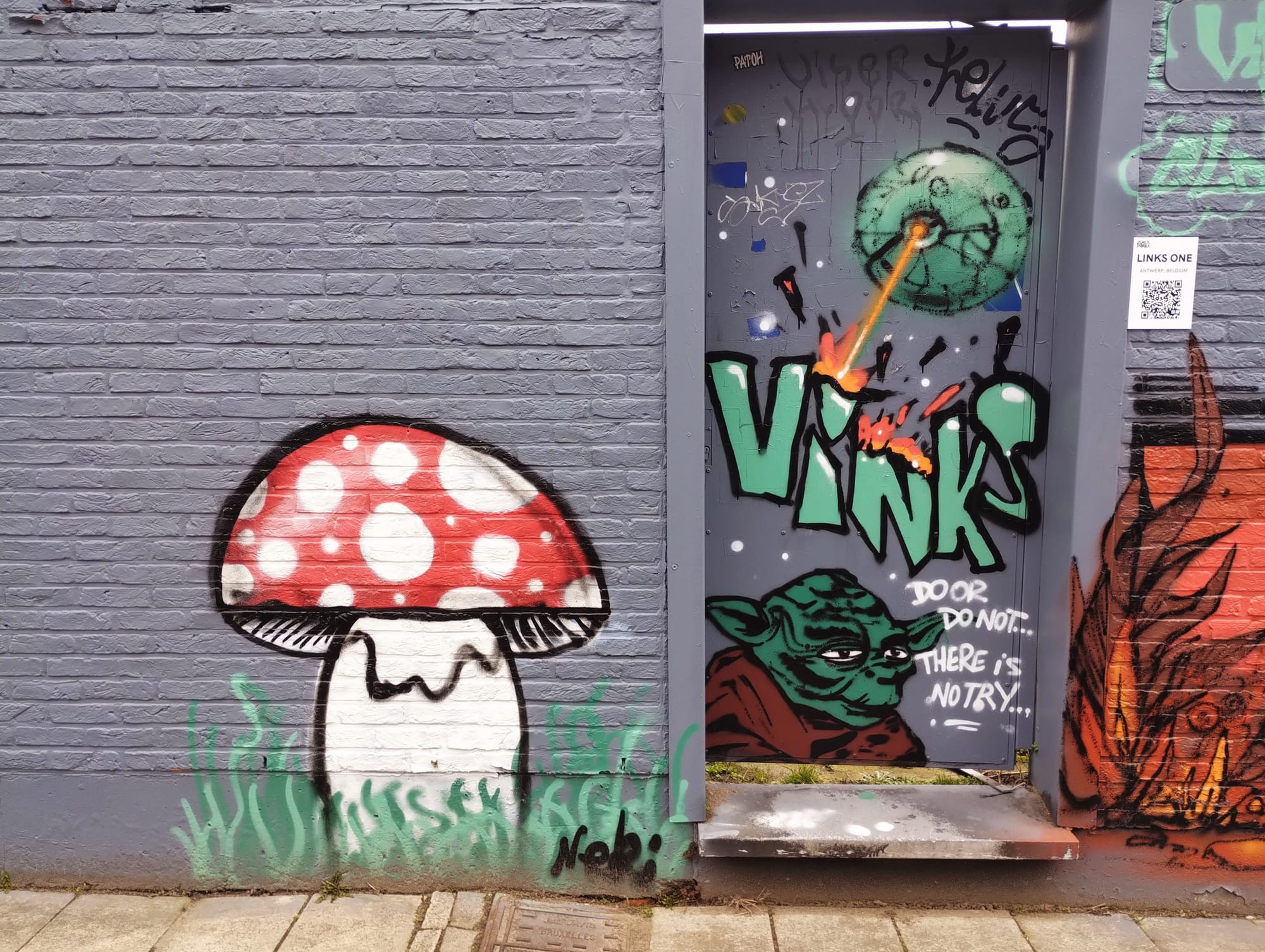 A brick wall with a large mushroom graffiti on the left side, painted with a red cap with white spots, a white stem, and green grass detail. Next to it, a doorway with graffiti art featuring a green planet with a laser, the word "VINKS", and a depiction of Yoda from Star Wars with the text "DOOR DO NOT... THERE IS NO TRY...". A QR code is visible on the right.