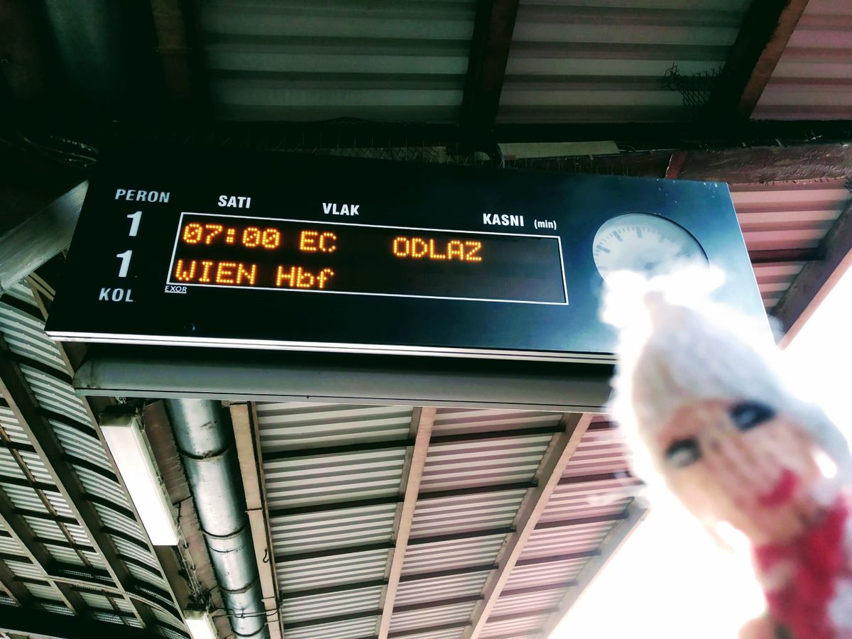 Train station information display showing the 07:00 Eurocity service to Wien Hbf, partially obscured by a flirty Peruvian finger puppet.