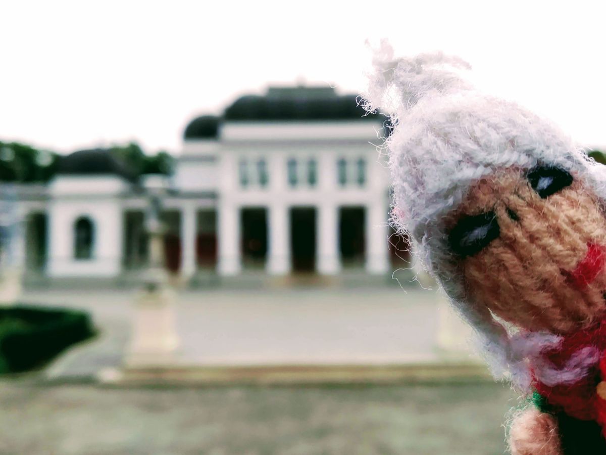 Finger puppet in front of a blurry white casino in Cluj-Napoca's central park.