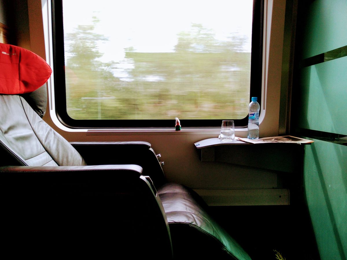 A black leather seat, a red antimacassar, and a finger puppet looking through a window at a blurry landscape. On a small shelf next to the window a glass of water.