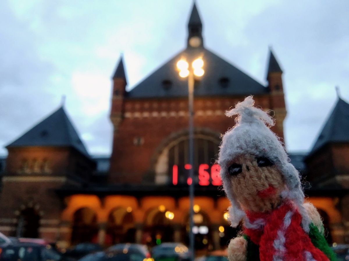 Puppet in front of a large red neon clock on Copenhagen's ornate railway station.