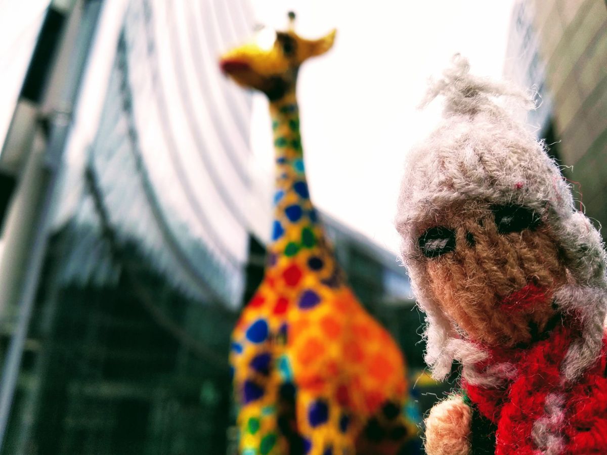 A staunchly magnificent finger puppet standing in front of a multi-coloured Lego giraffe.