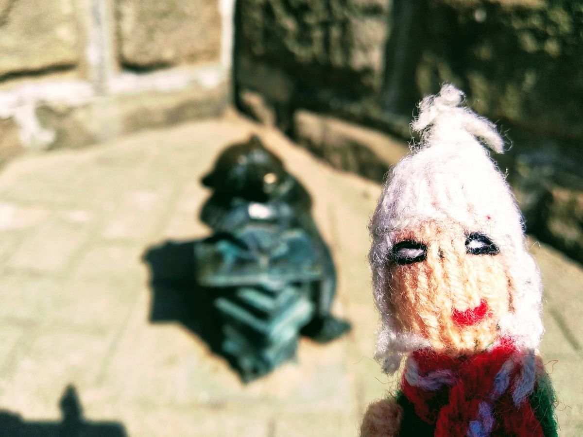 Triumphant finger puppet in front of a small bronze statue of a bear leaning on a pile of books.