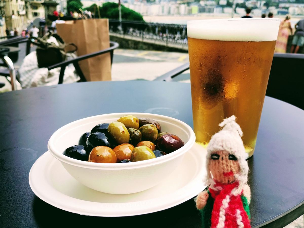 An insatiable finger puppet prepares to devour a glass of cold refreshing beer and a selection of olives.