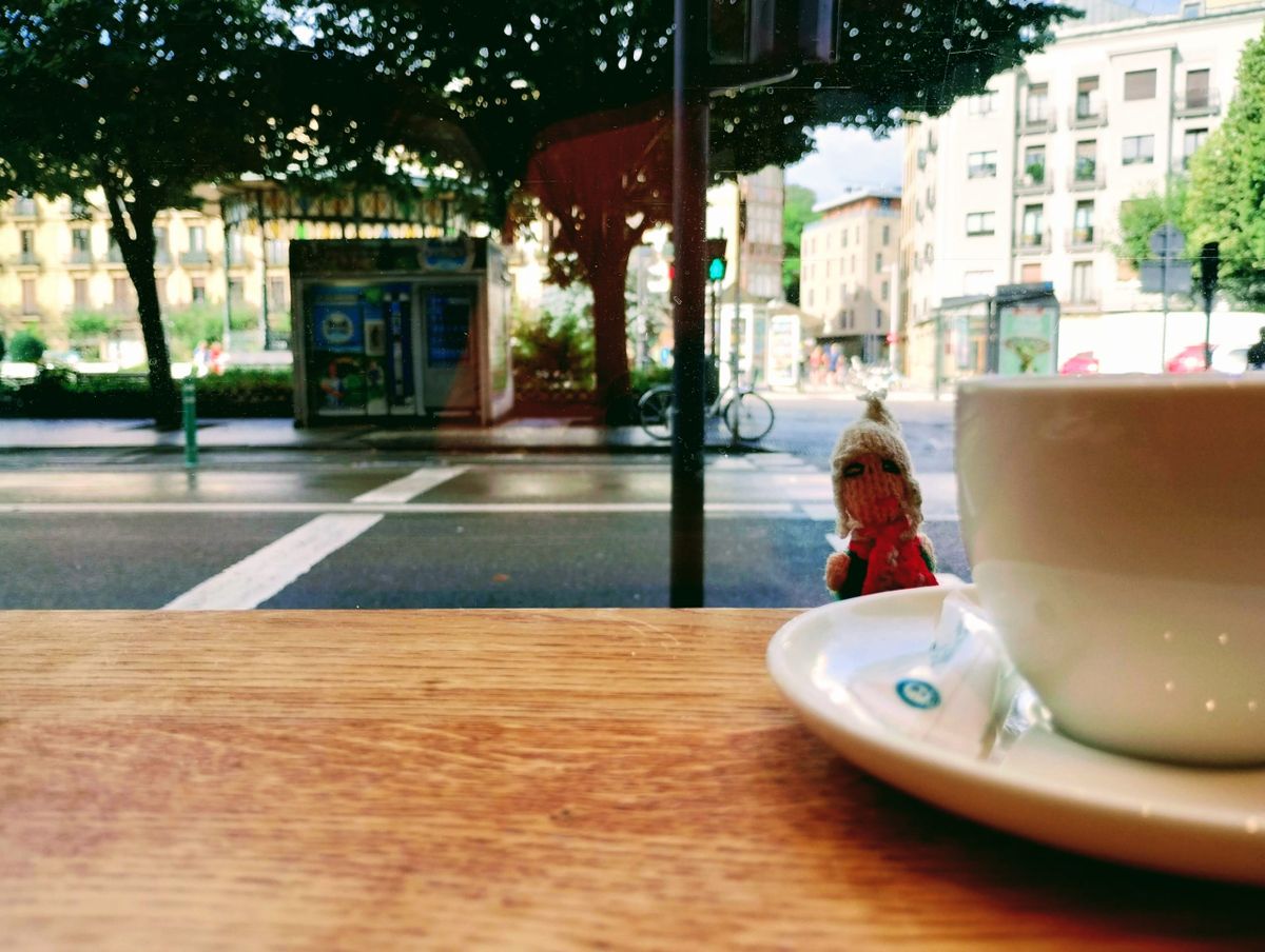 A finger puppet eyes a cup of coffee from behind a counter top.