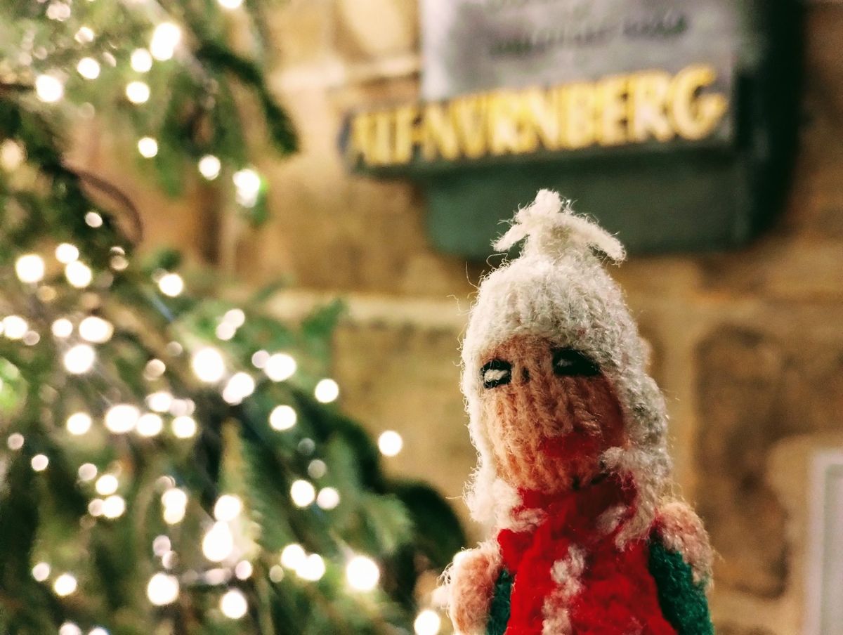 An innocent Peruvian finger puppet huddles eagerly in front of a Christmas tree.