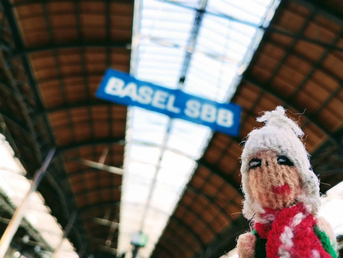 Excited Puppet standing under a blue Basel SBB station sign.