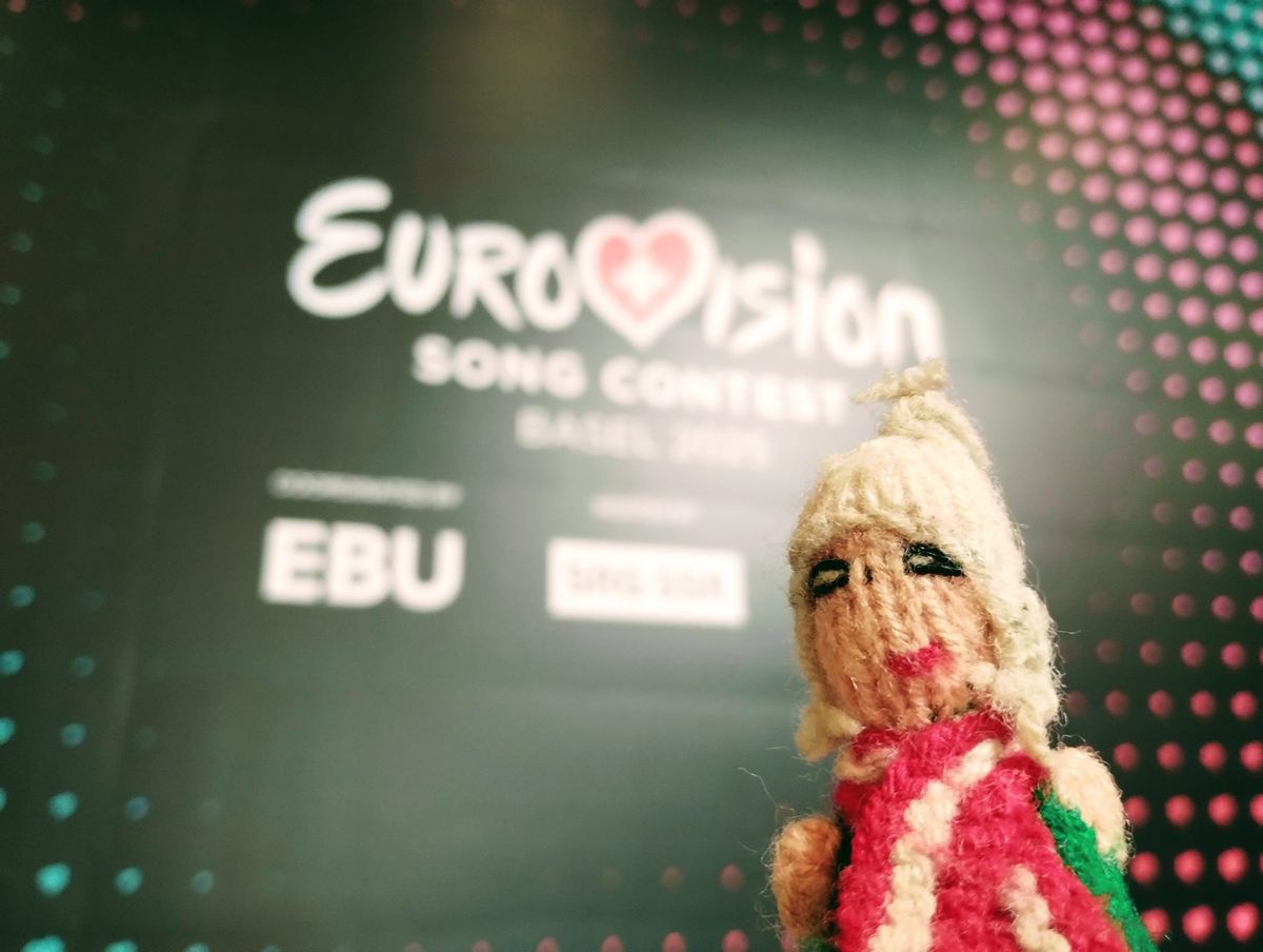 A proud finger puppet standing in front of a blurred Eurovision Song Contest logo.