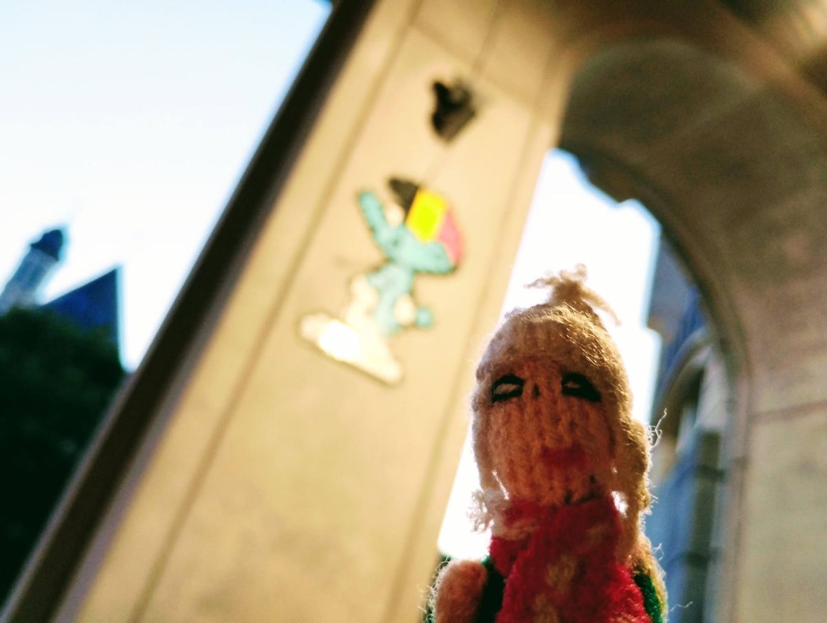 Smug Finger puppet in front of a mosaic of a Smurf wearing a hat in the colours of the Belgian flag.