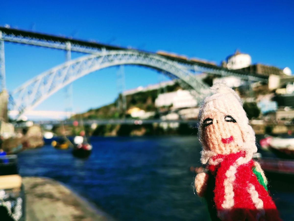 Nautical finger puppet overlooking the river Douro with the Dom Luís I Bridge in the background under a bright blue sky.