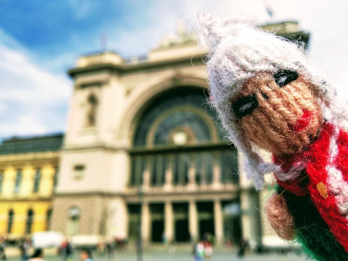 A mucky pup(pet) with food on its scarf, in front of the arched entrance to Budapest Keleti train station.