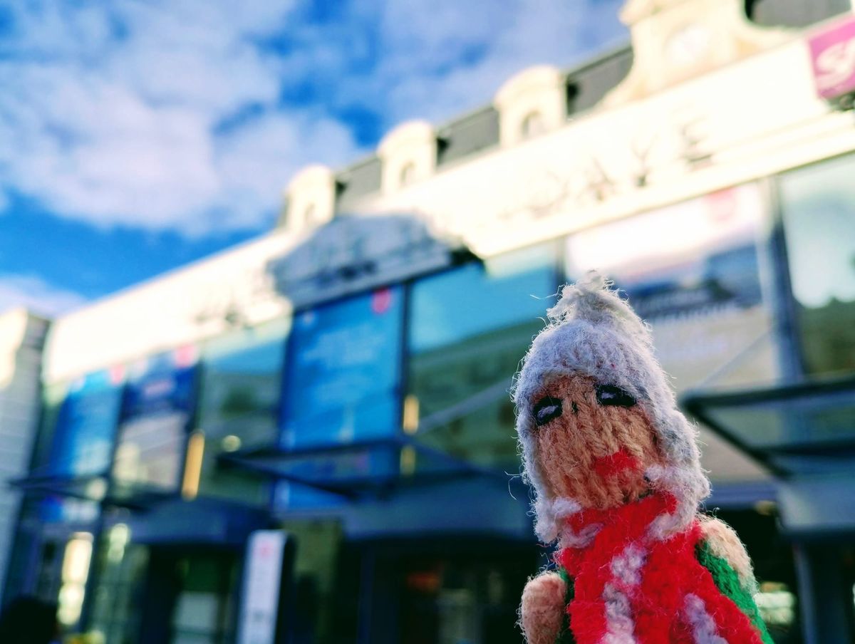 Finger puppet posing in front of the railway station in Hendaye against a blue sky.