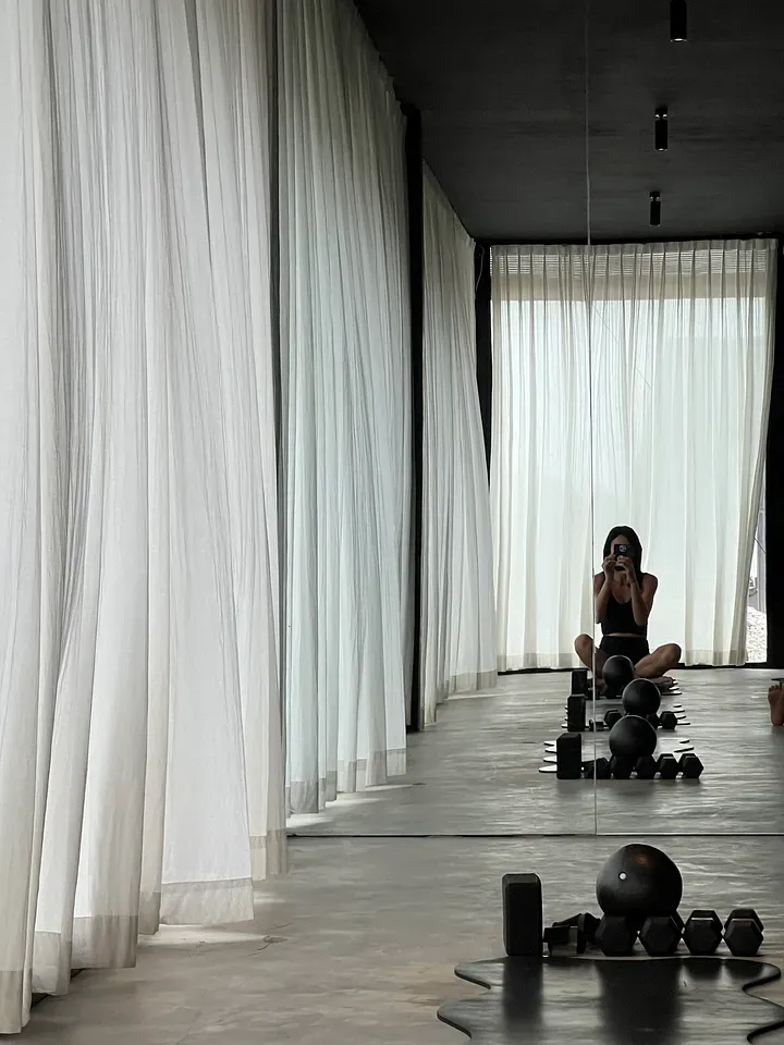 Mirror selfie in The Pilates Project mat studio, with sheer white curtains and black weights and balls