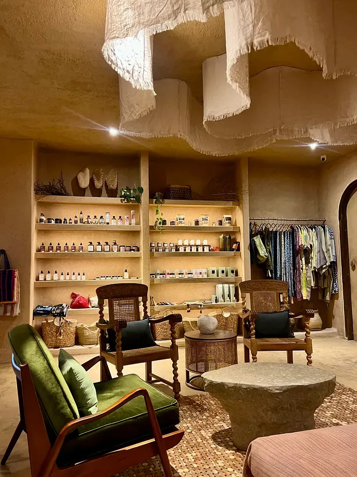 Therapy Day Spa reception with wooden chairs, a green velvet armchair and shelves of skincare under draped fabric