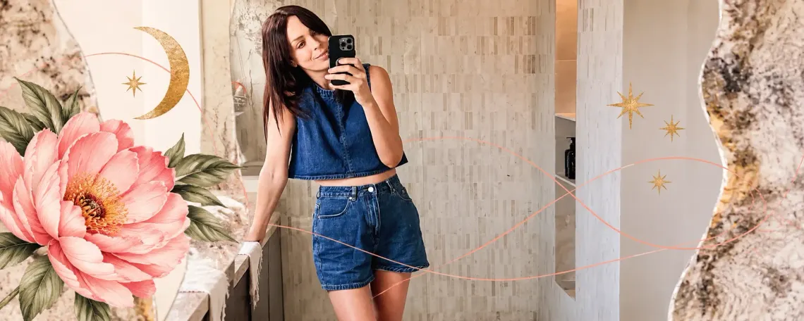 Stevie taking a mirror selfie in a denim crop top and shorts in a marble bathroom, framed by an illustrated peony, gold crescent moon and stars