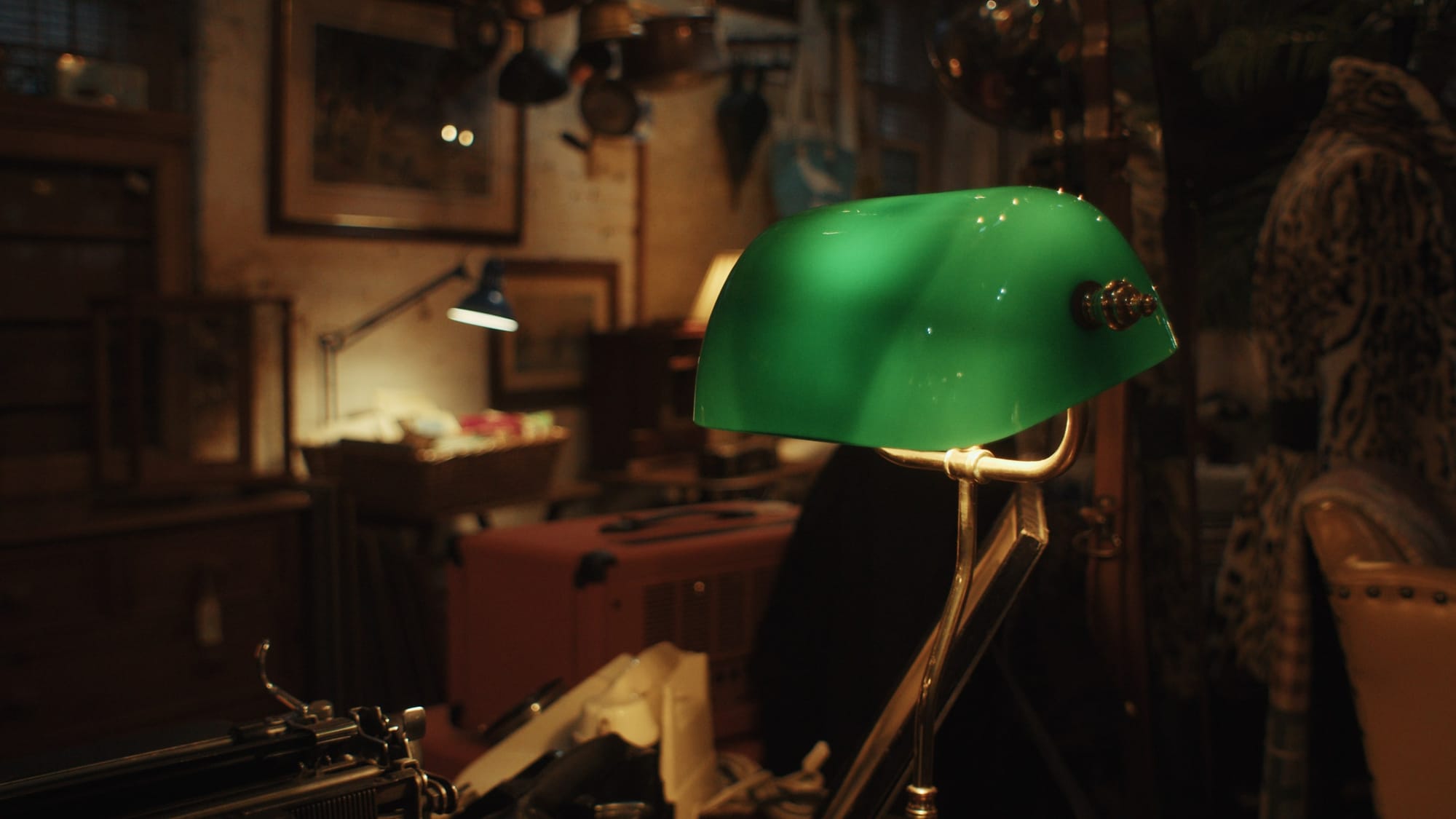 A vintage green banker’s lamp glows inside Courtyard Antiques, surrounded by typewriters, furniture, and eclectic objects