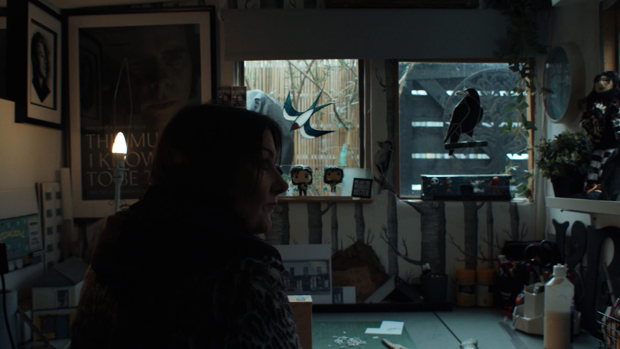A woman sits in a cosy craft studio with model buildings and art supplies